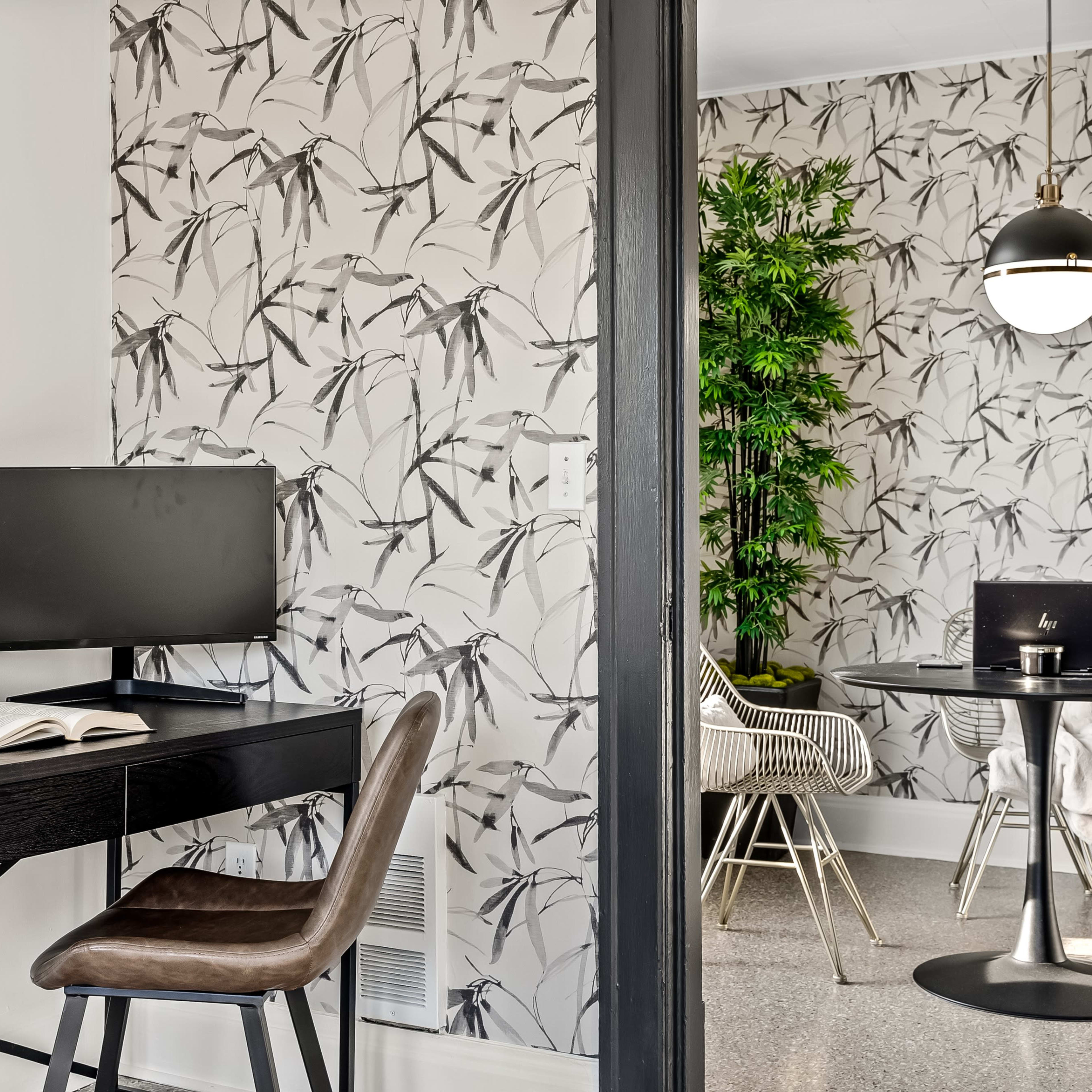 A workspace with a computer desk and a chair is visible, leading to a cozy seating area adorned with a plant and a small round table.