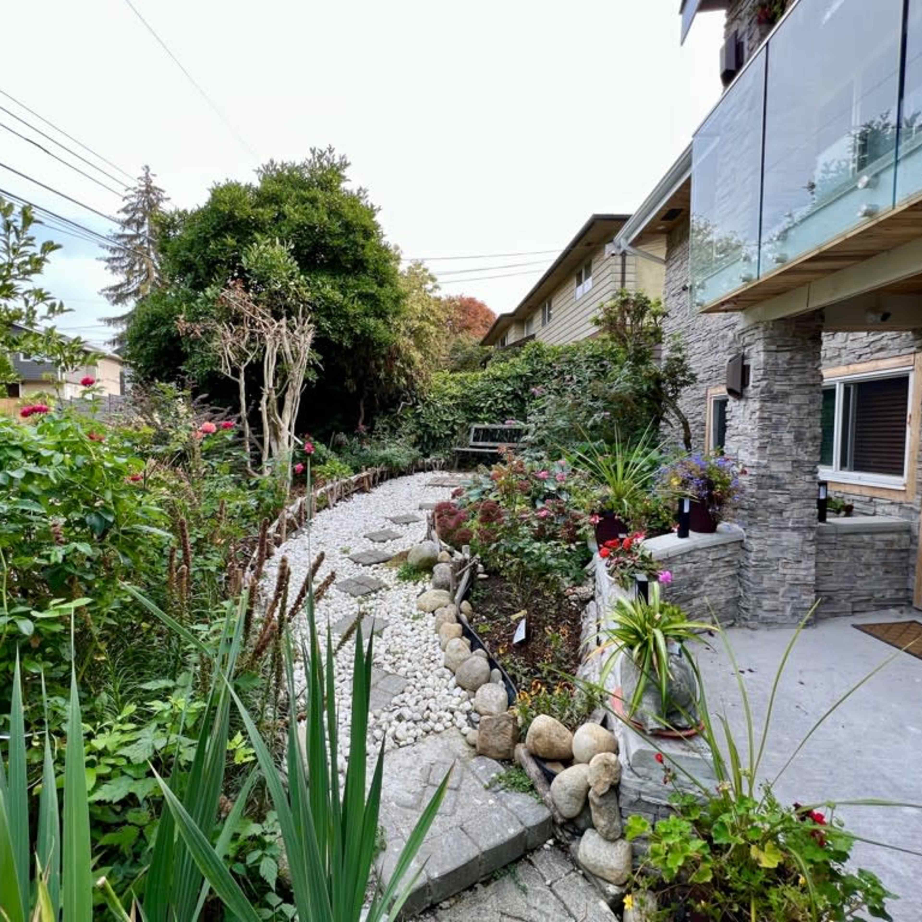 A landscaped garden path with stones and greenery leads to a modern house with a stone facade.