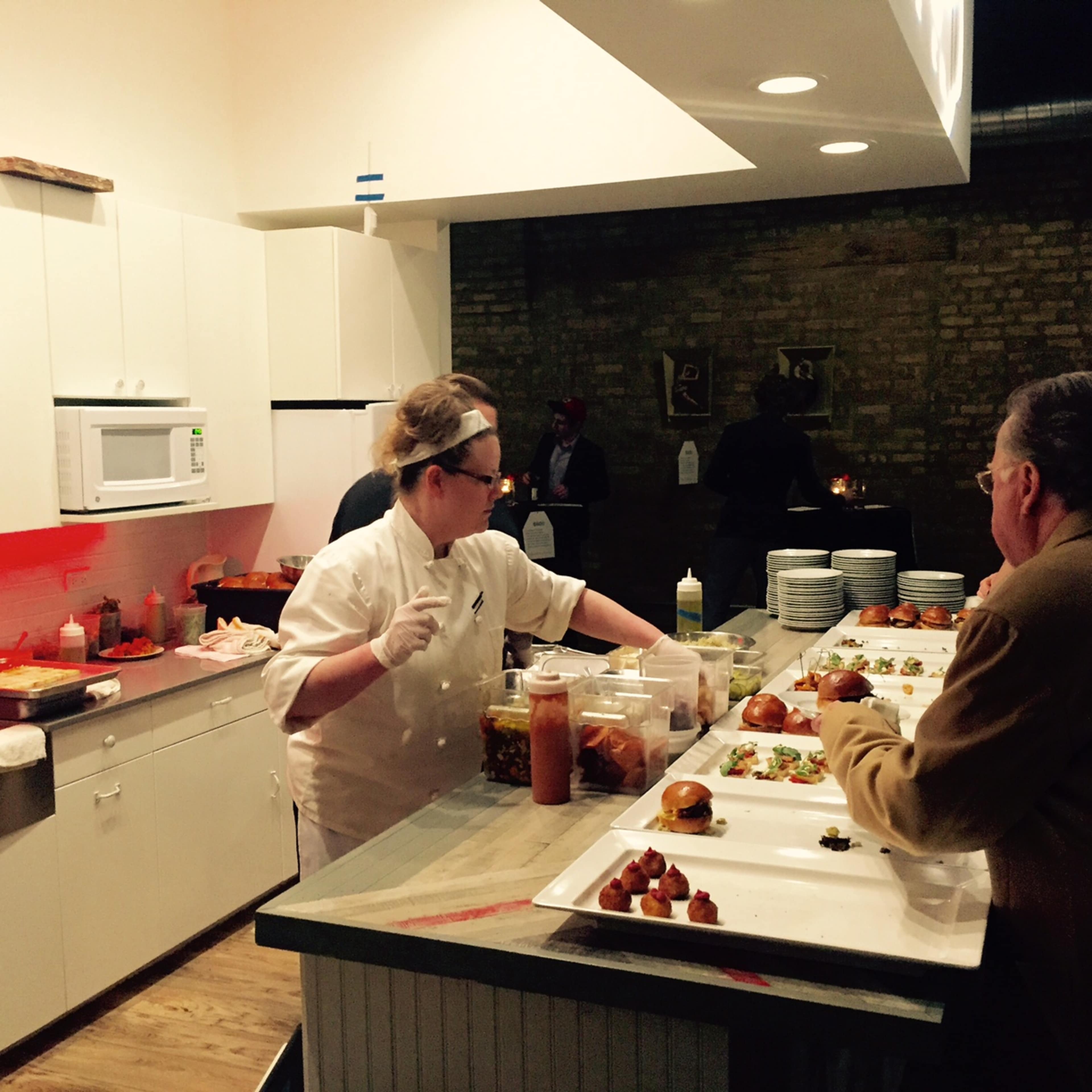 A chef prepares food in a modern kitchen while a customer observes from the counter.