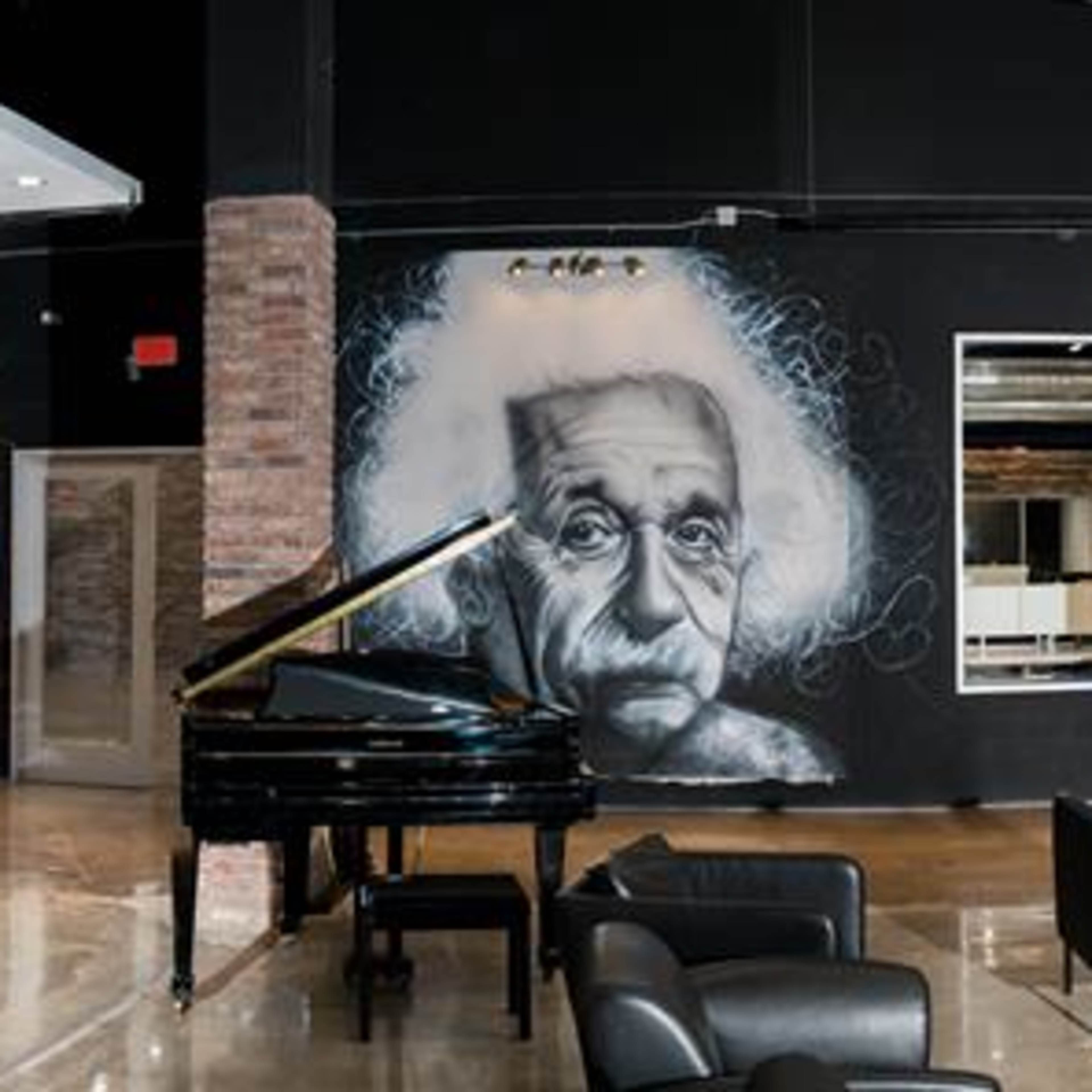 A stylish interior space featuring large murals of Bob Marley, Albert Einstein, and a woman, along with modern furniture and a grand piano.
