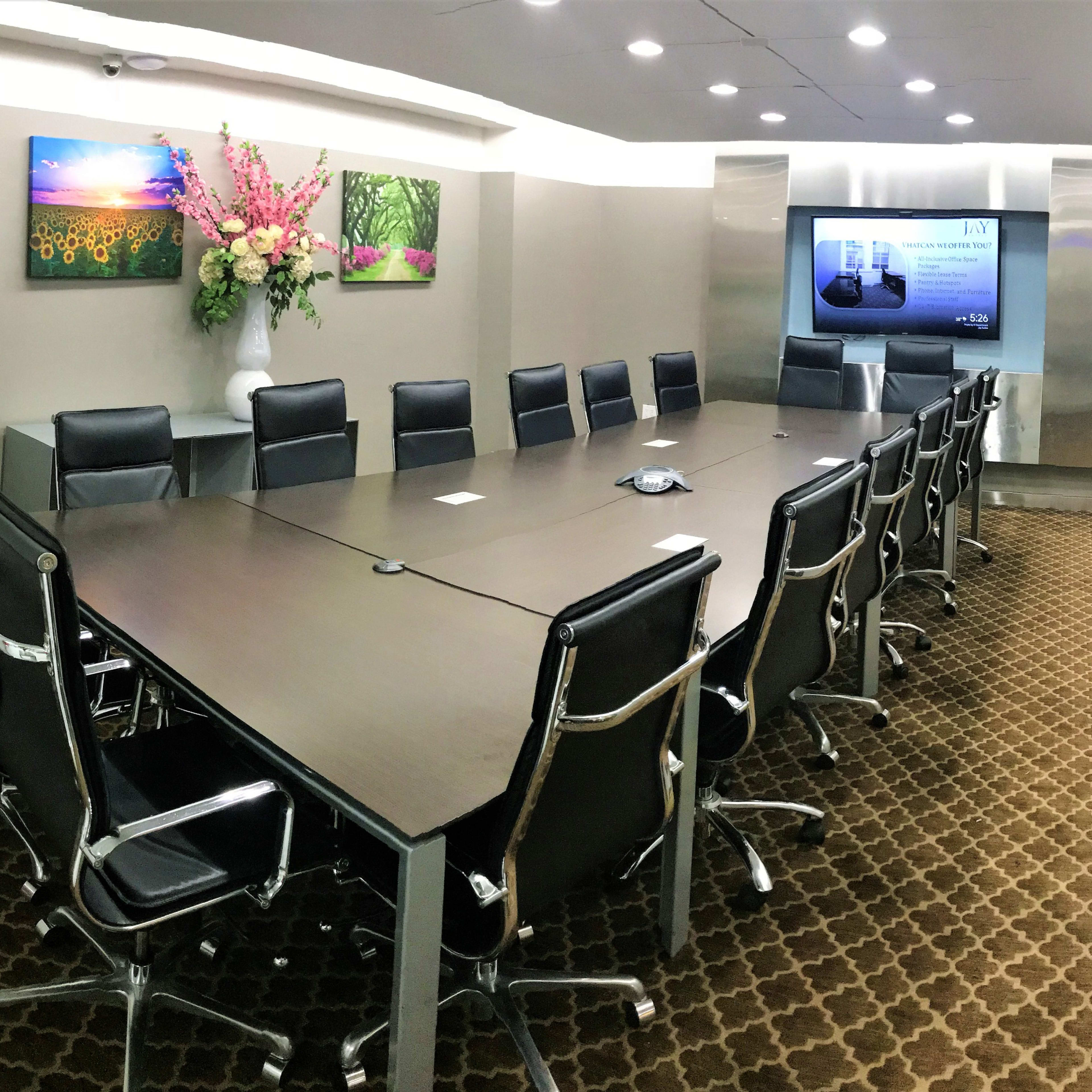 A large conference room features a long table surrounded by black leather chairs, with modern artwork on the walls and a television screen at one end.