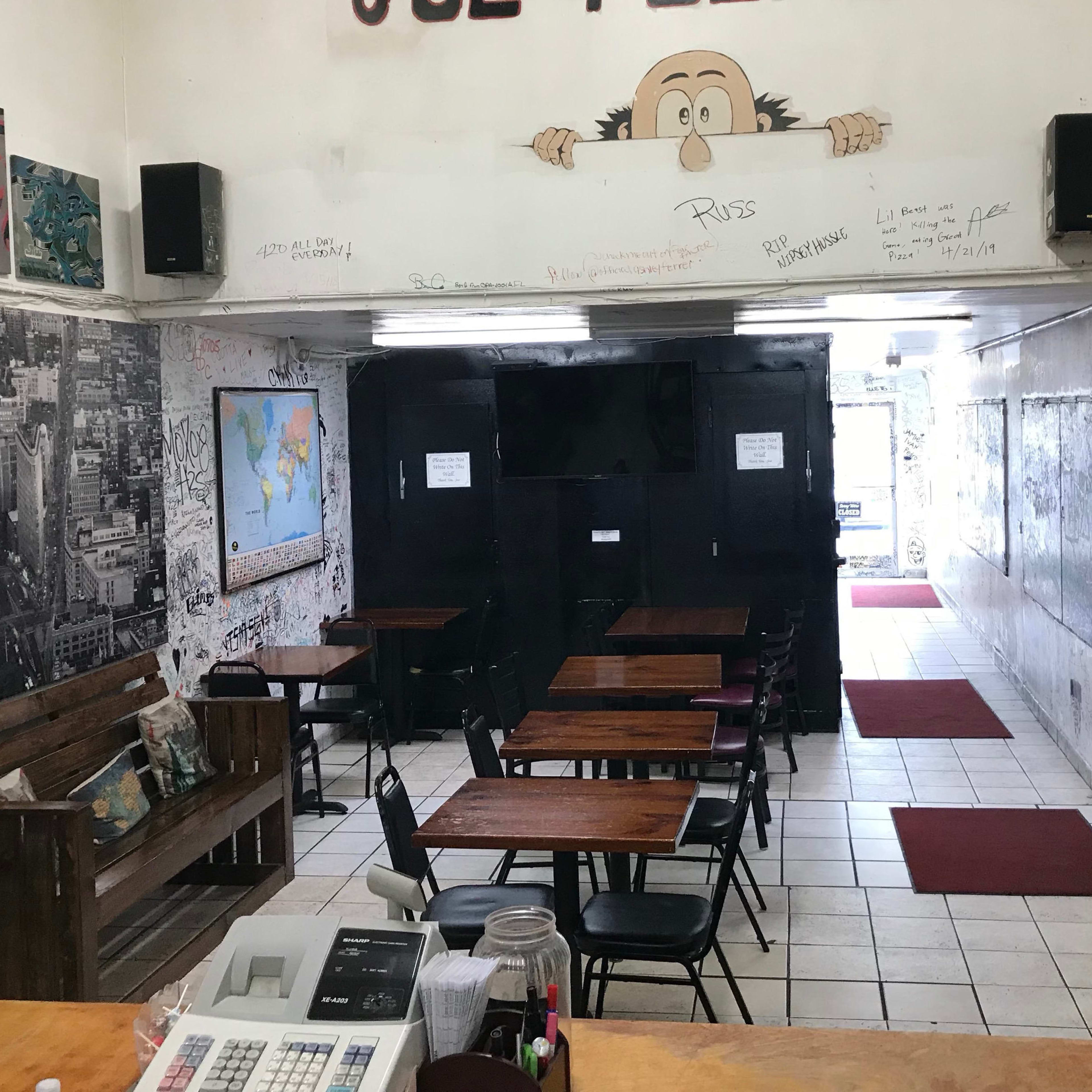 A small, partially decorated café with wooden tables, black chairs, and walls covered in graffiti.