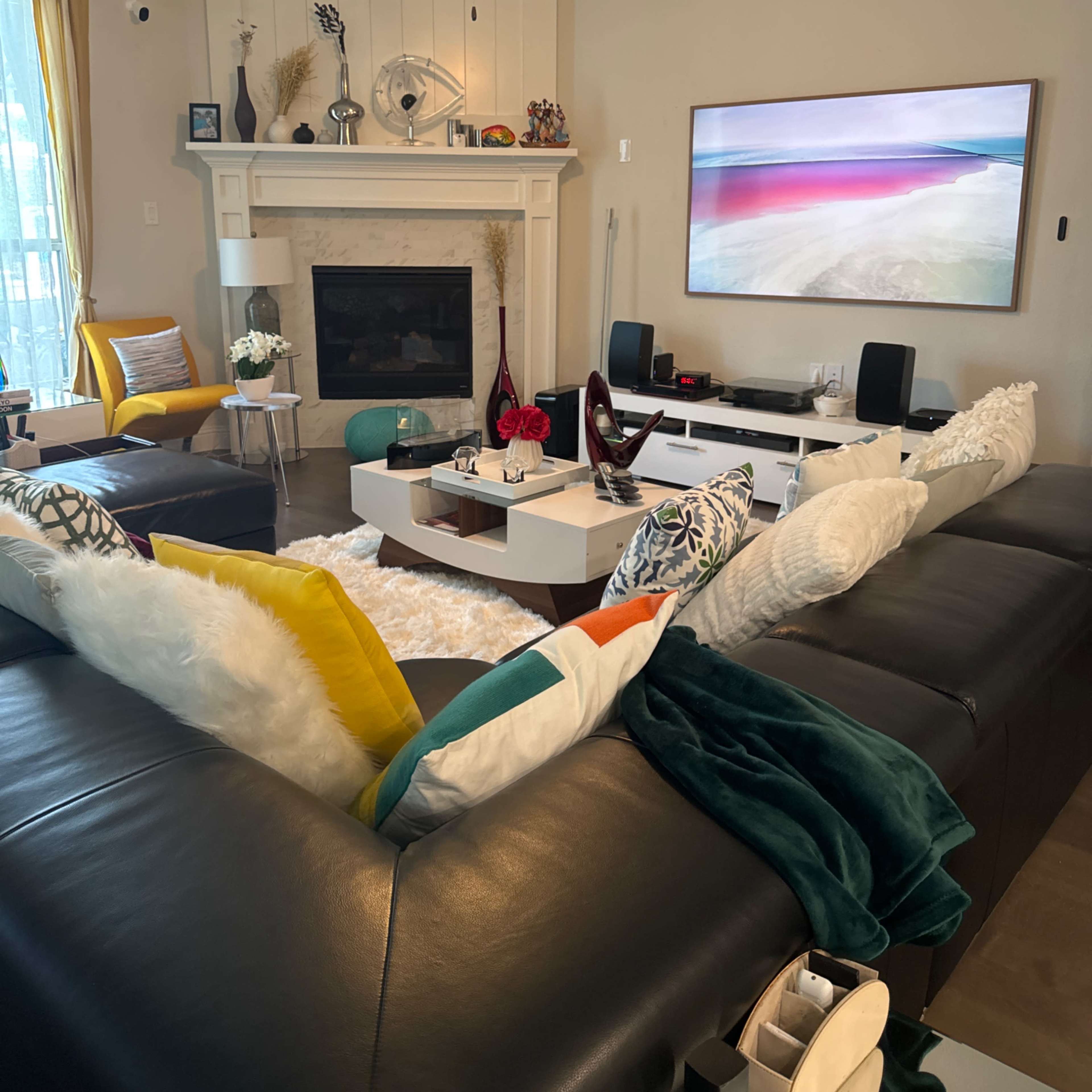 A modern living room featuring a sectional sofa, a coffee table, a fireplace, and a large TV mounted on the wall.