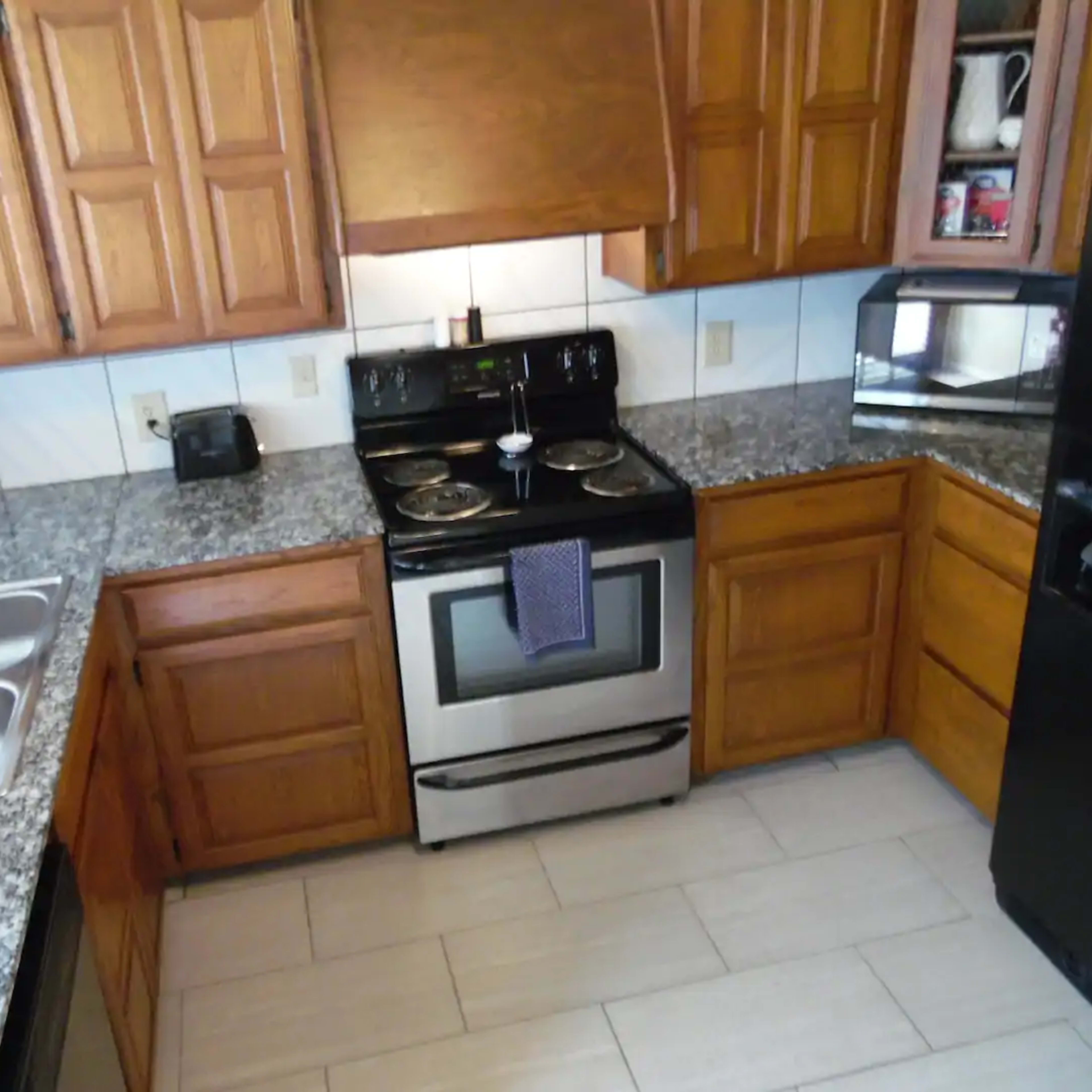 A kitchen with wooden cabinets, a stainless steel stove, a silver microwave, and a two-basin sink on a granite countertop.