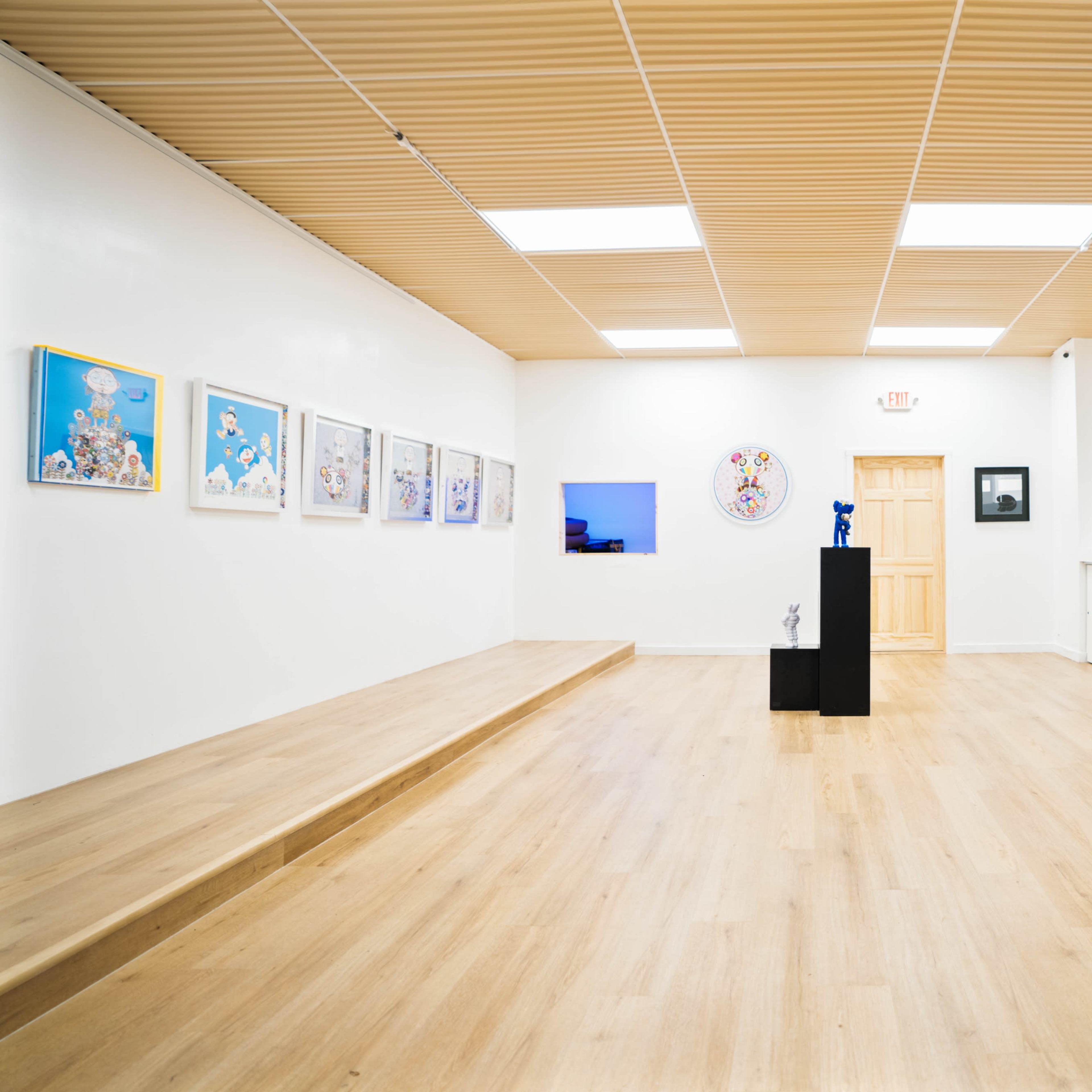 An art gallery featuring an array of framed artworks on the white walls and a central black pedestal displaying a sculpture.
