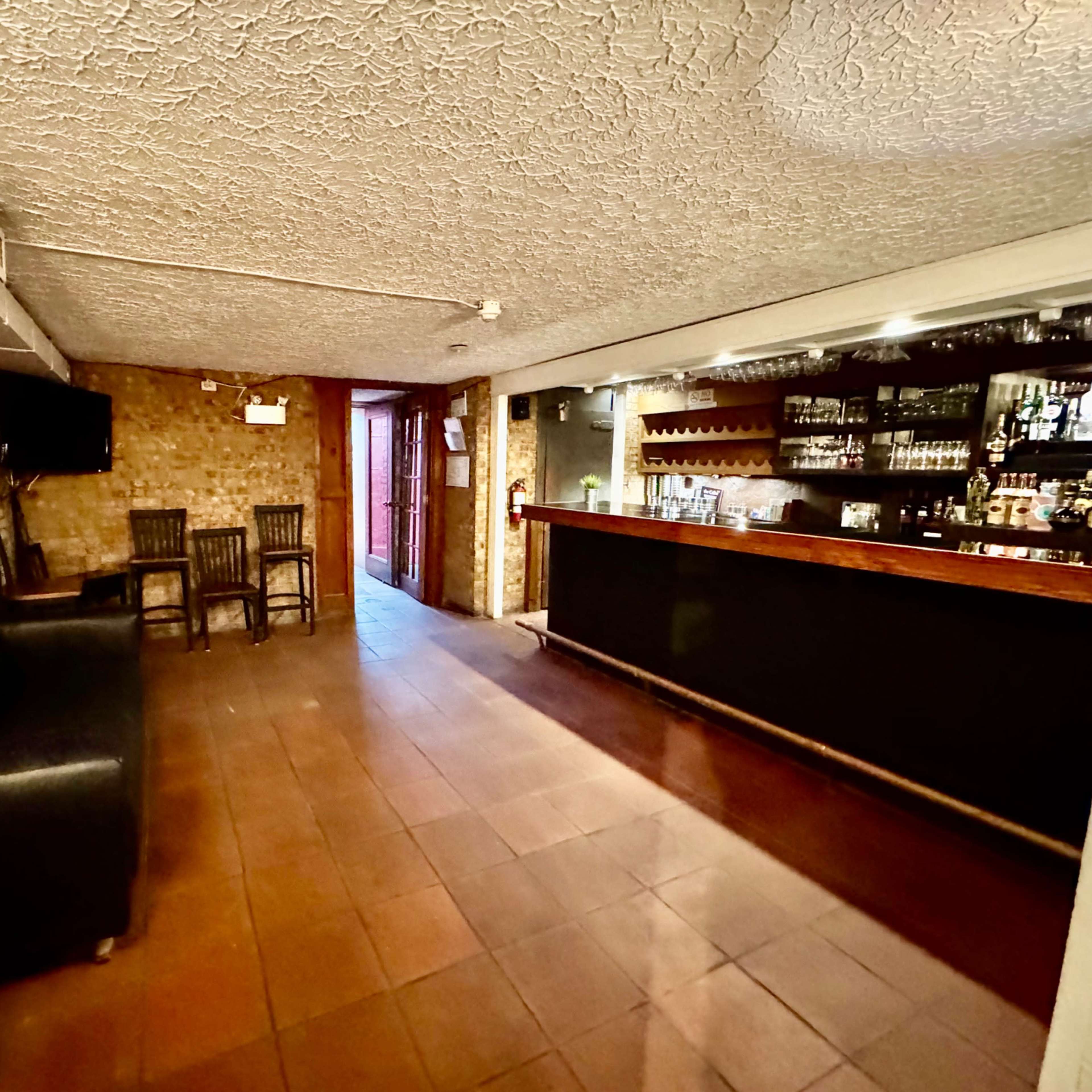 A spacious bar area with a dark countertop, several chairs, and a doorway leading outside.