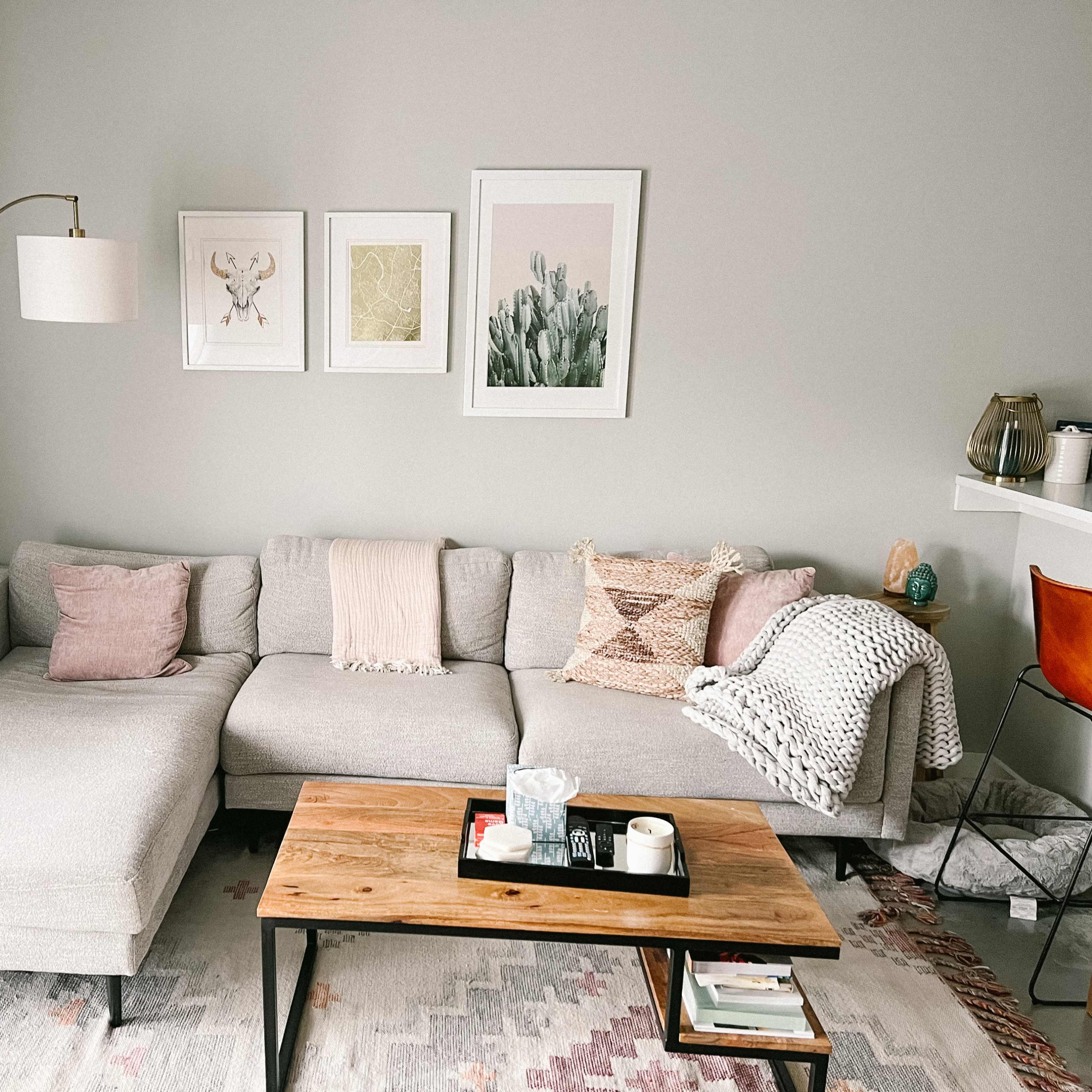 A modern living room features a gray sectional sofa with decorative pillows, a wooden coffee table, and framed artworks on the wall.