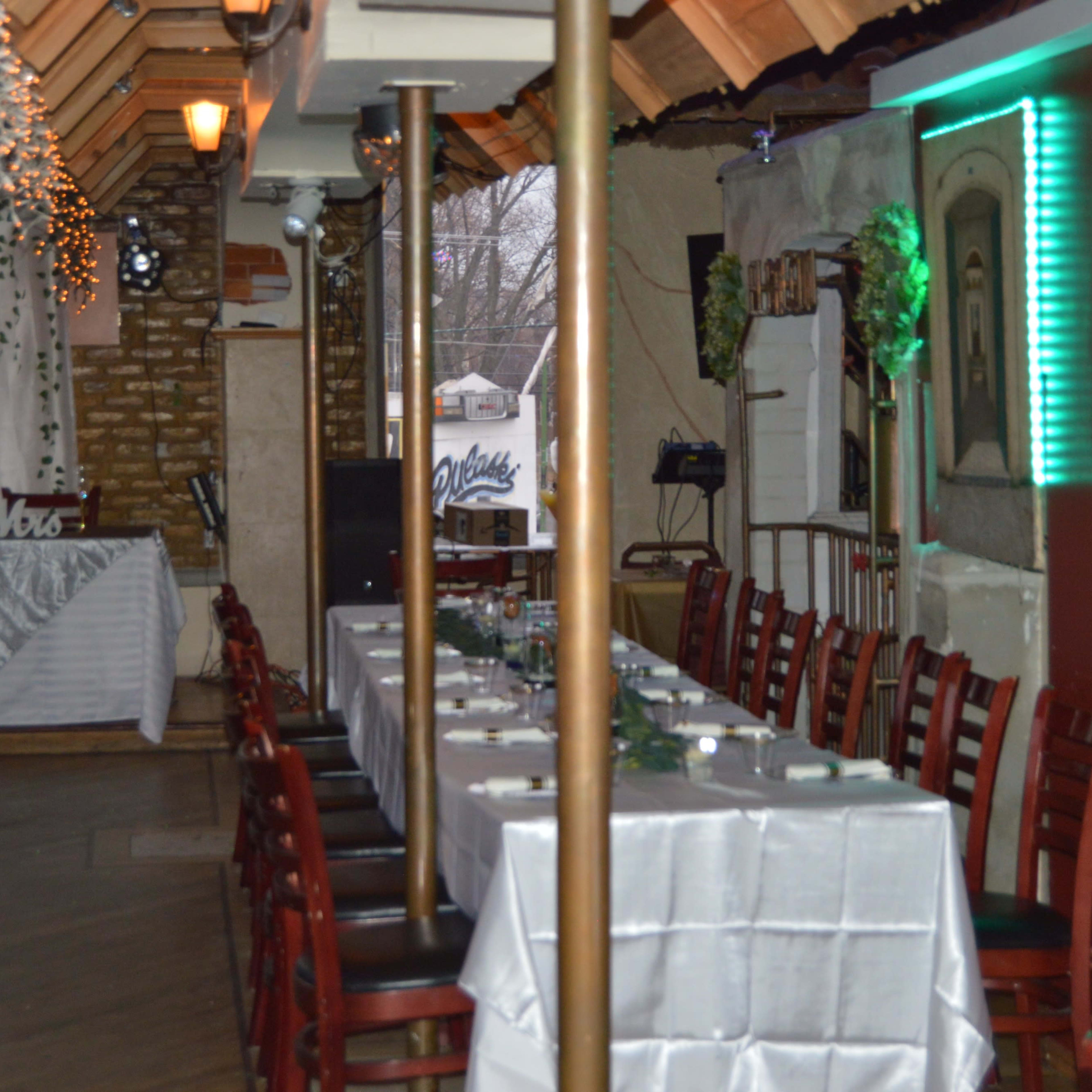 An indoor dining area with a long table set for a meal, decorated with white tablecloths and surrounded by red chairs, beneath a sloped ceiling.