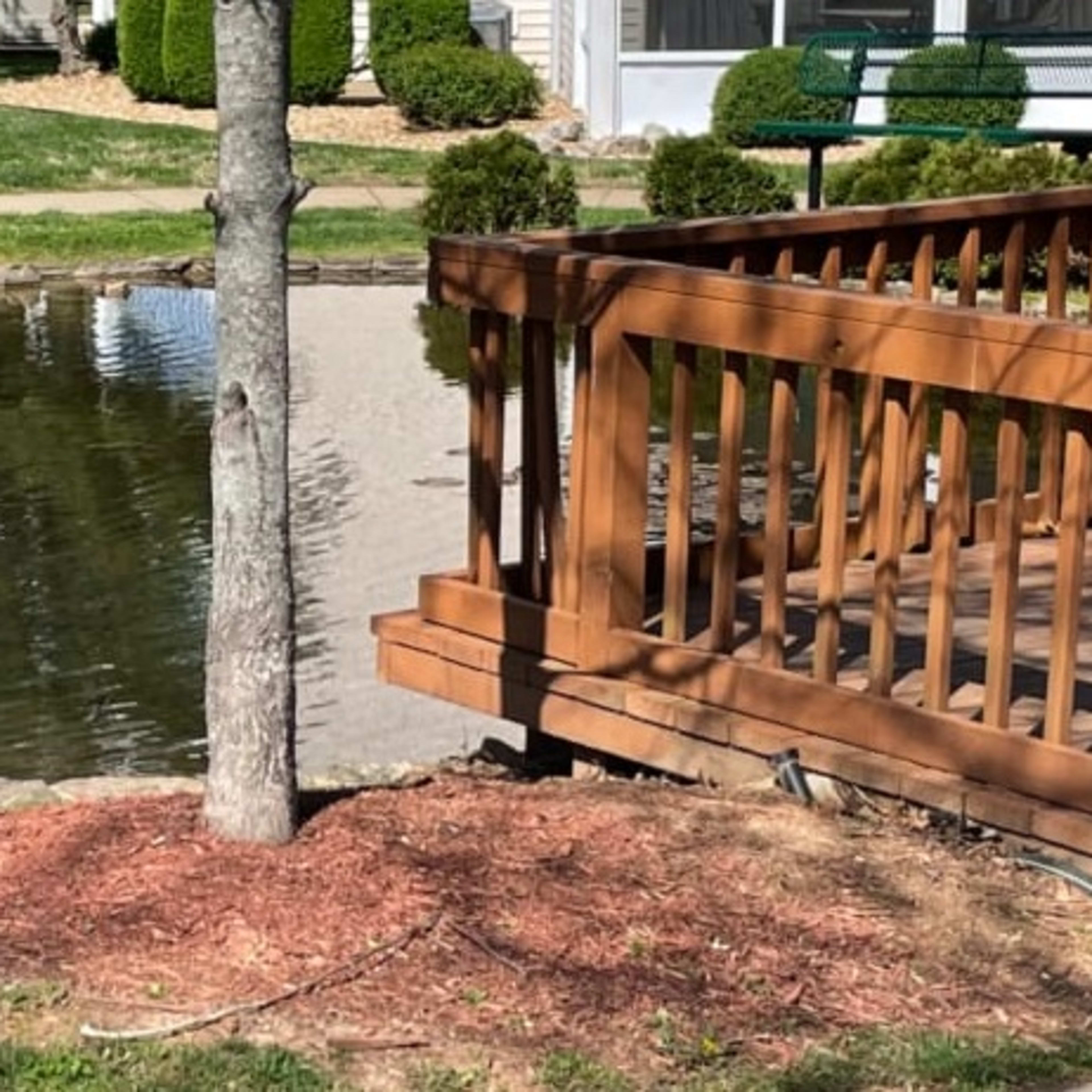 A wooden deck overlooks a pond surrounded by grass and landscaping features.