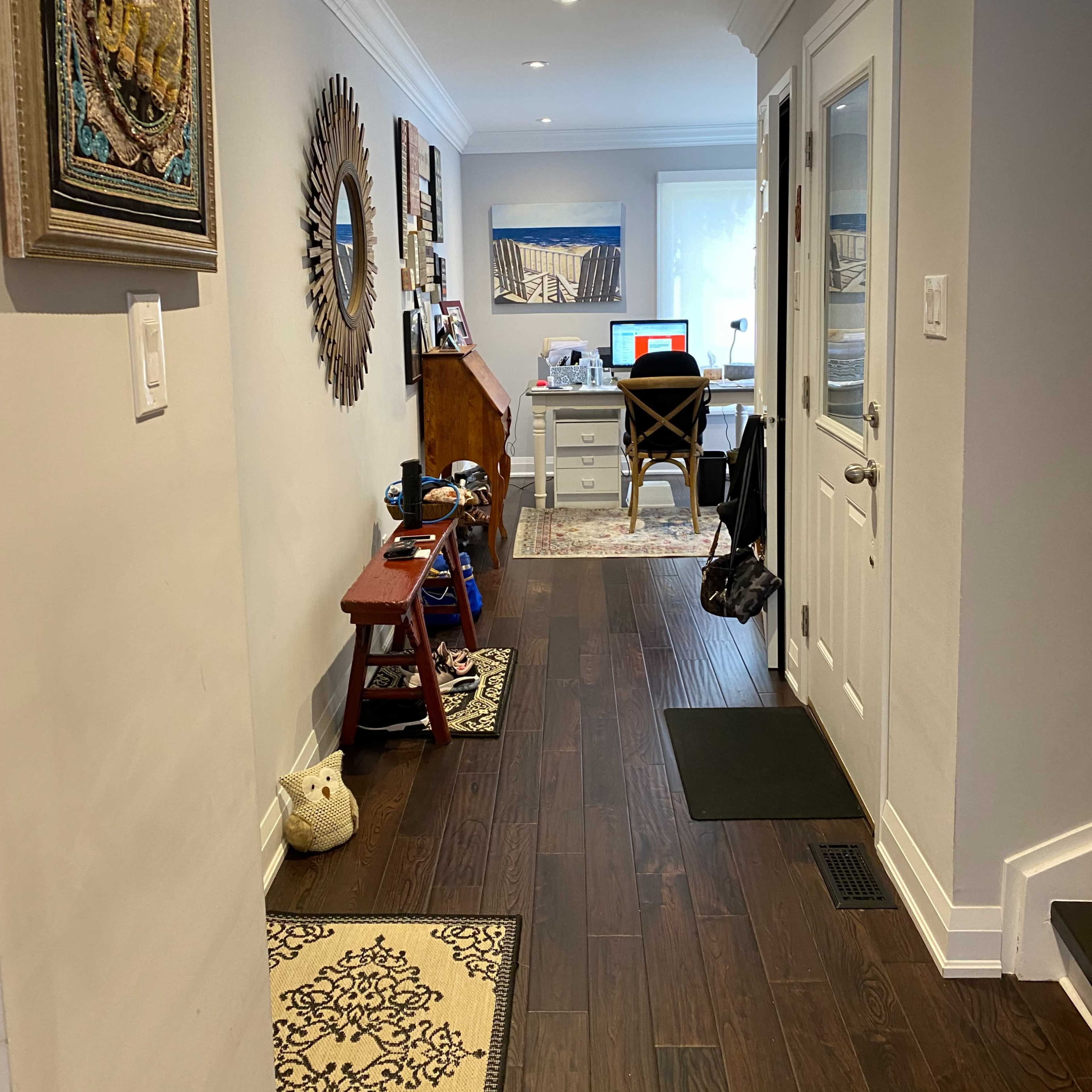 A hallway leads to a home office, featuring wooden flooring, a desk, and decorative items along the walls.