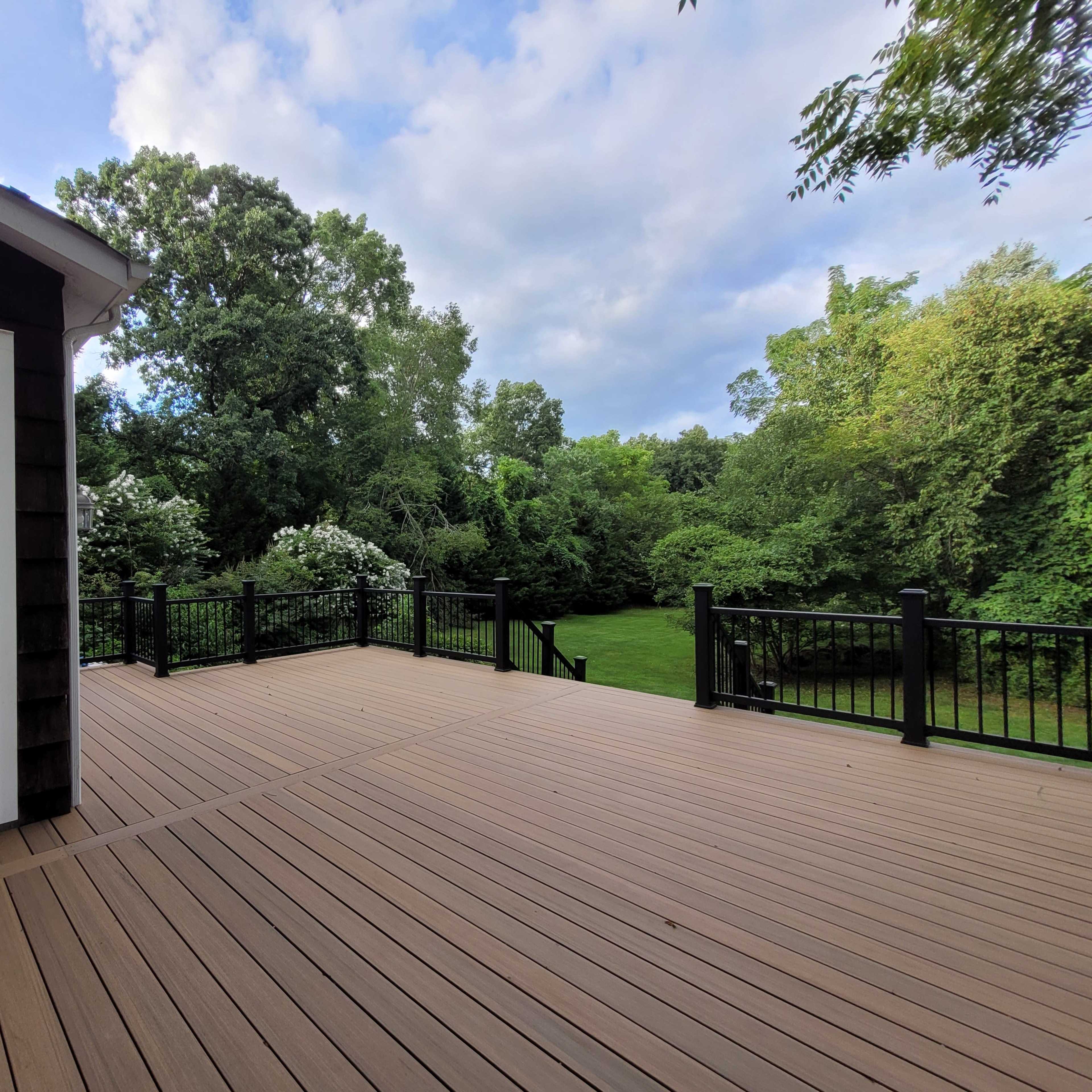 A spacious wooden deck overlooking a green lawn surrounded by trees and foliage.
