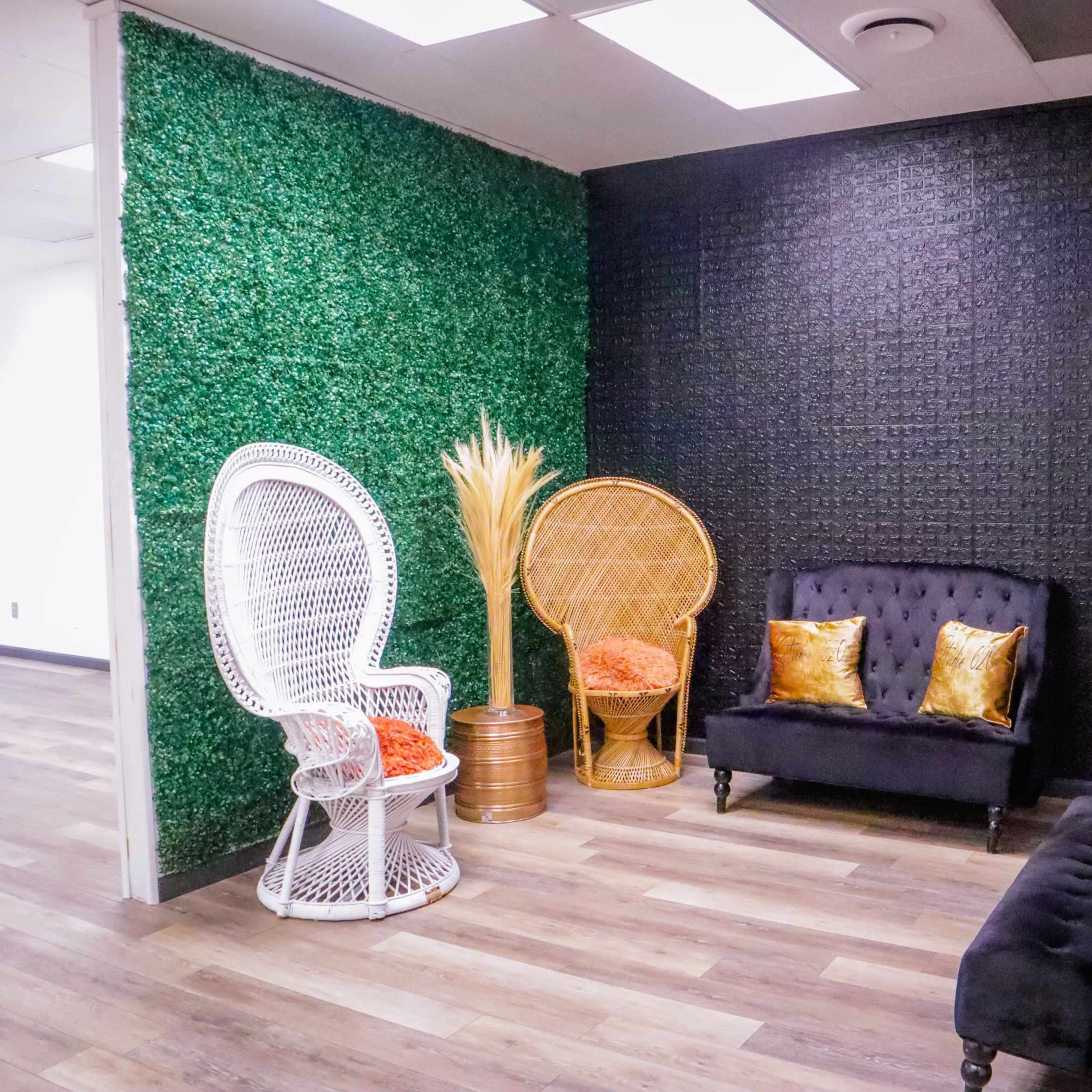 A modern lounge area with green and black textured walls, featuring two decorative seating options and a small table with a plant arrangement.
