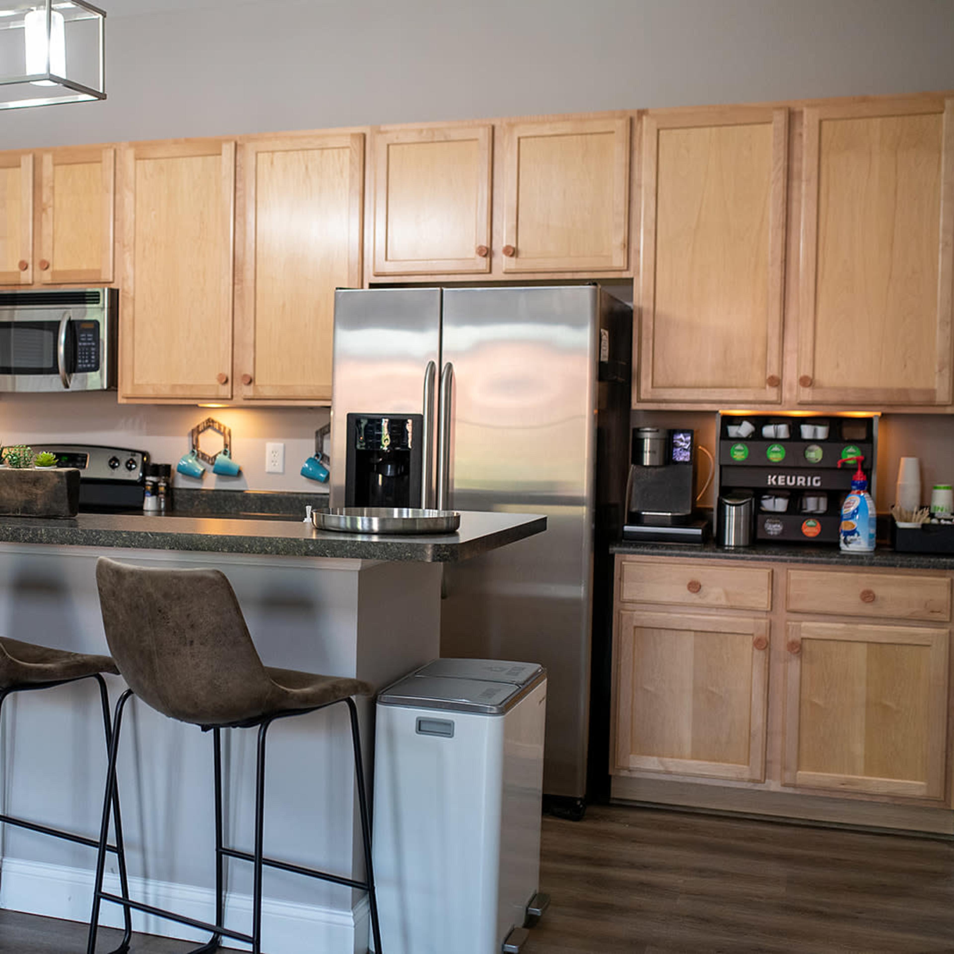 A modern kitchen with wooden cabinets, stainless steel appliances, a large island with seating for four, and a wall-mounted light fixture.