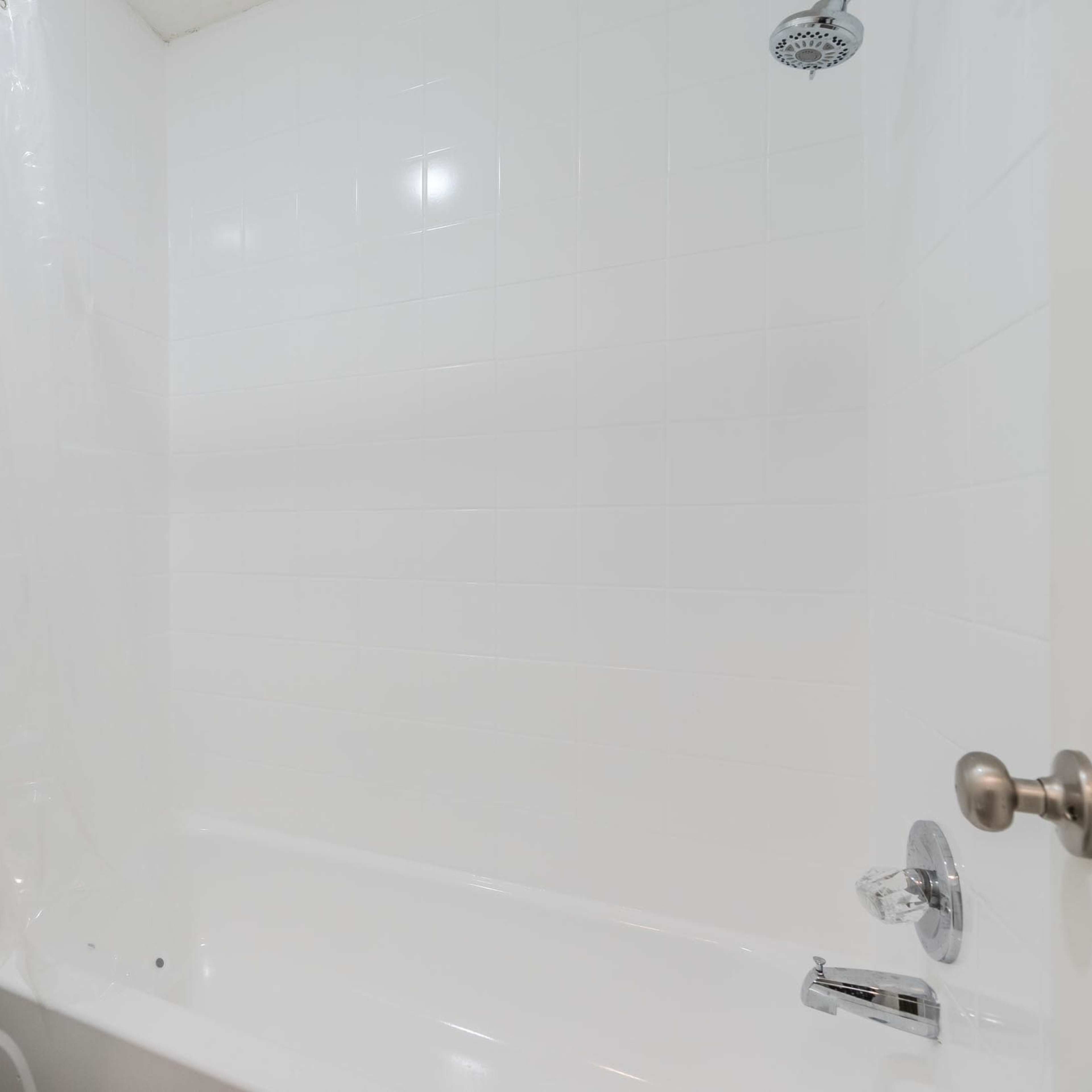 A clean bathroom with a white bathtub, toilet, and a shower curtain in a tiled shower area.