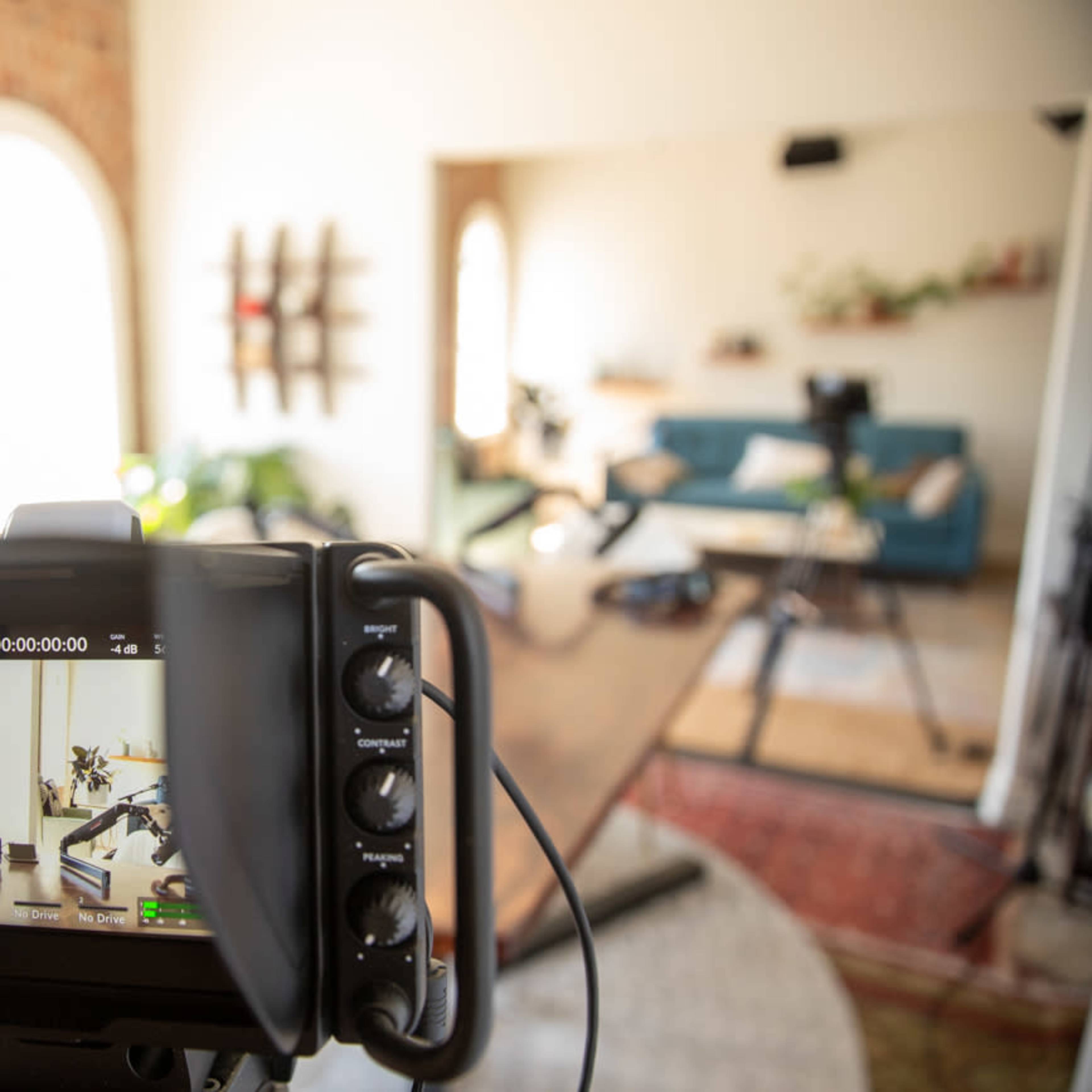 A camera is focused on a well-decorated interior space with plants, a large table, and a blue sofa.