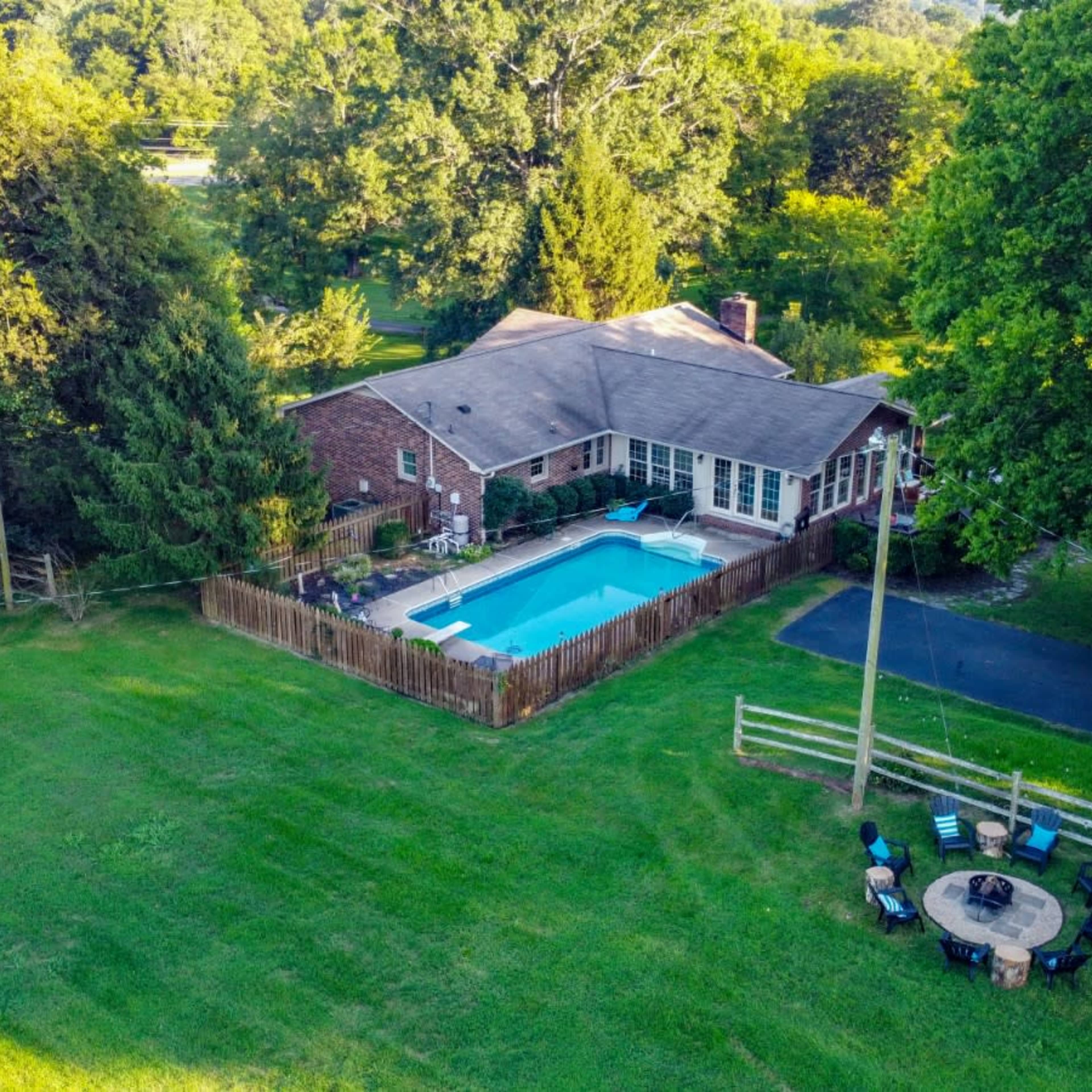 A single-story brick house with a swimming pool in the backyard, surrounded by a wooden fence and dotted with trees.