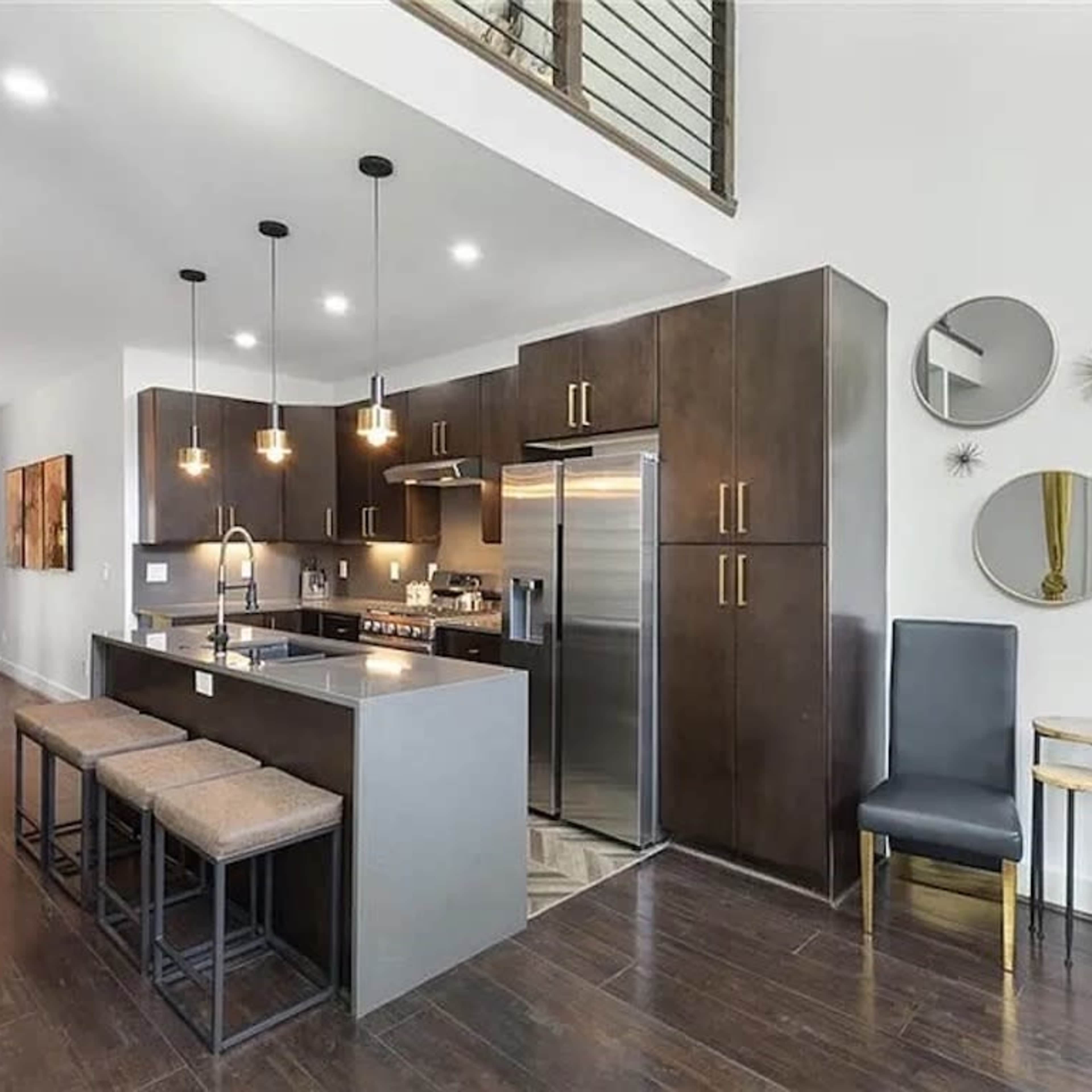 A modern kitchen with dark cabinets, a stainless steel refrigerator, and a large island with seating for four.