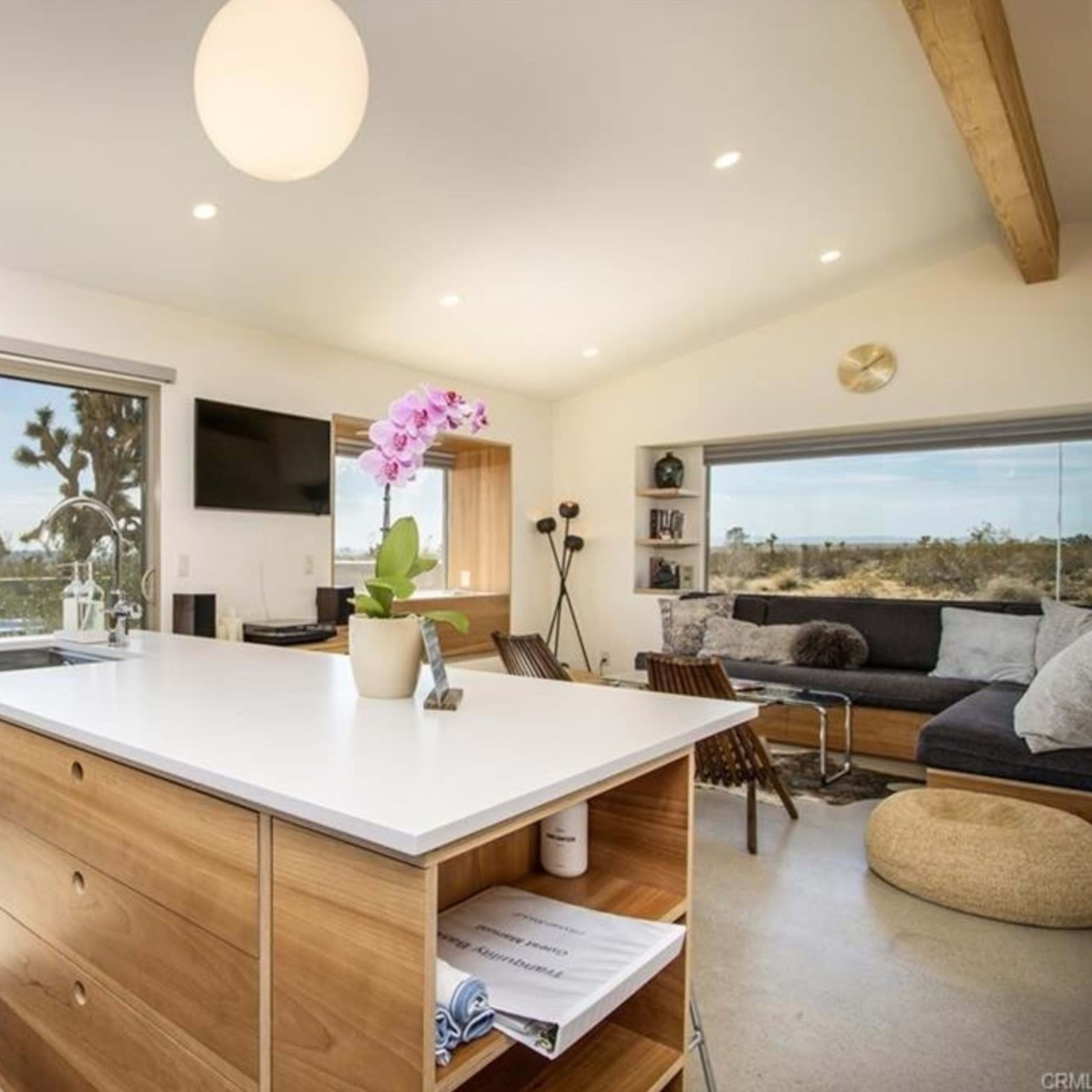 A modern kitchen with a central island, large windows showcasing a desert view, and a seating area with a couch and small table.