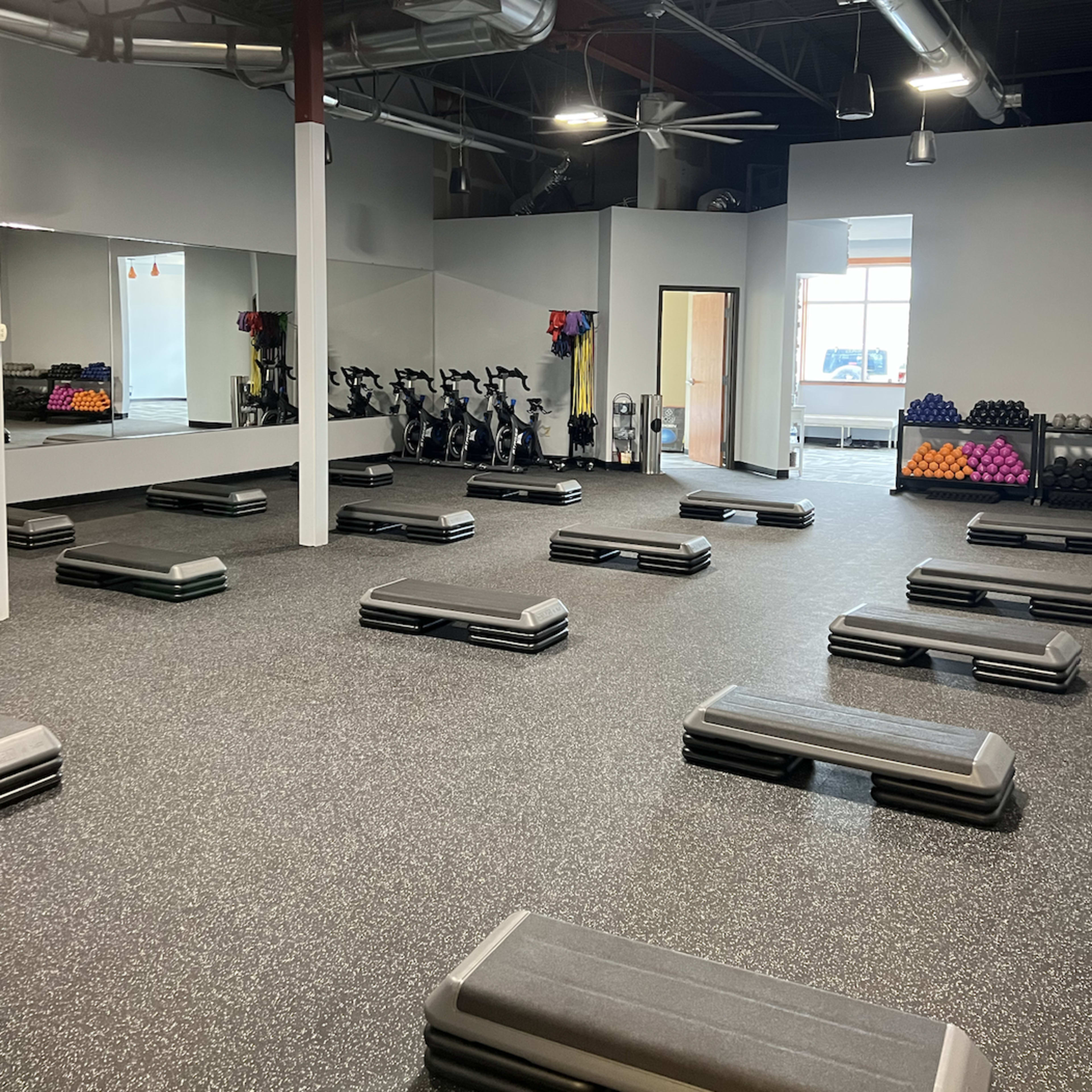 An empty gym space featuring multiple workout benches arranged in rows, with exercise equipment and weights visible in the background.