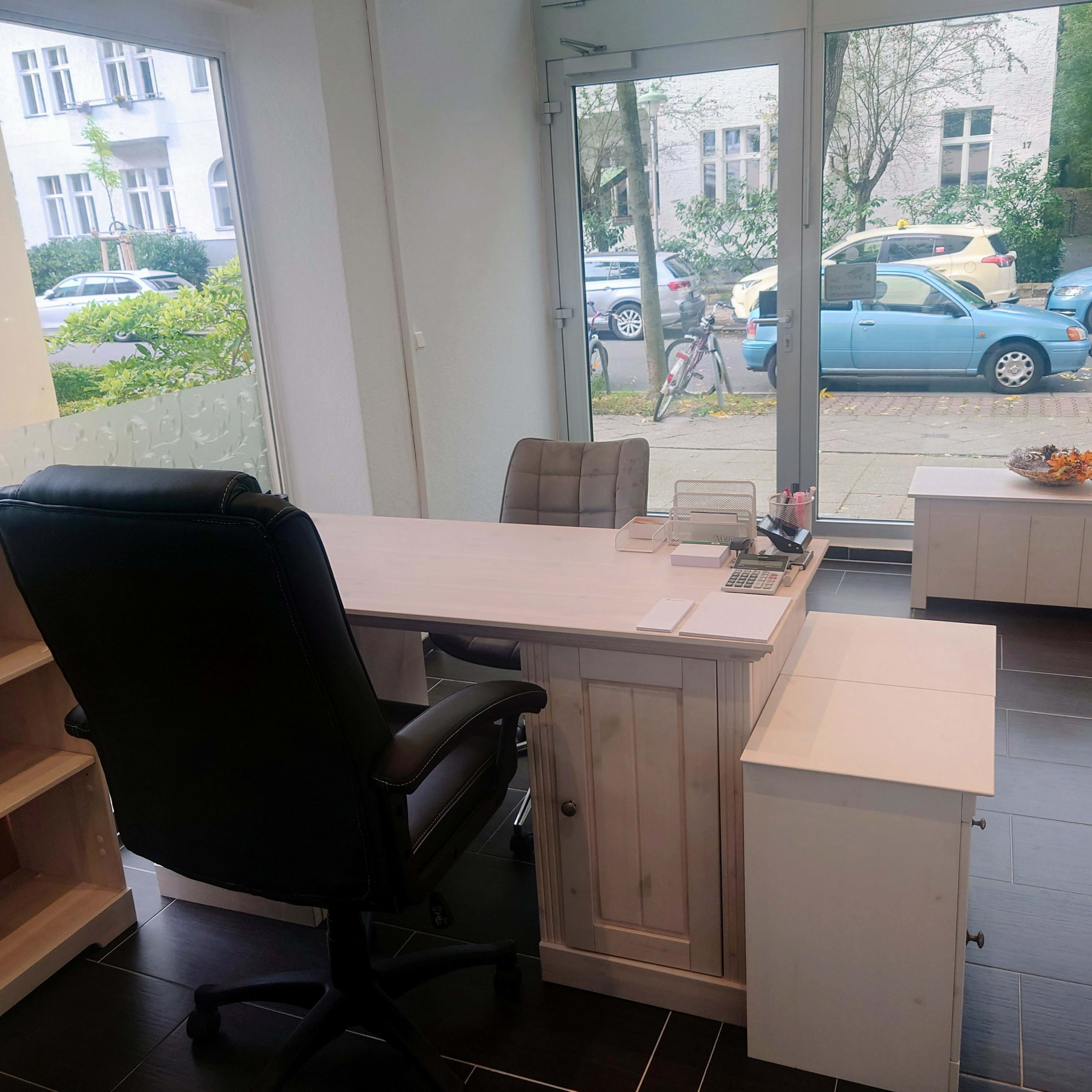A modern office space with a large desk, a black office chair, and minimalist furniture, featuring a window view of a street with parked cars.