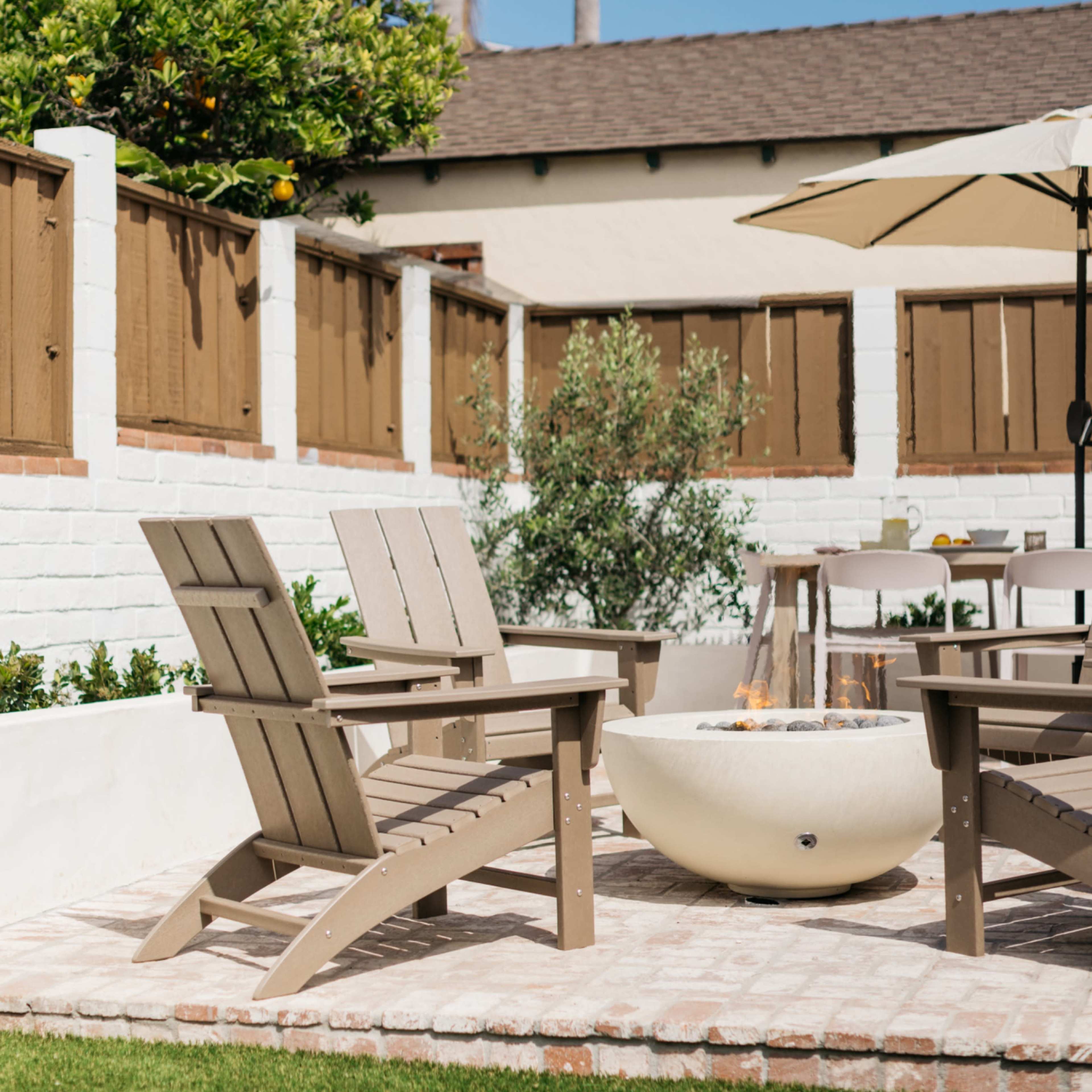 A cozy backyard features wooden Adirondack chairs arranged around a fire pit, with a patio umbrella and greenery surrounding the area.