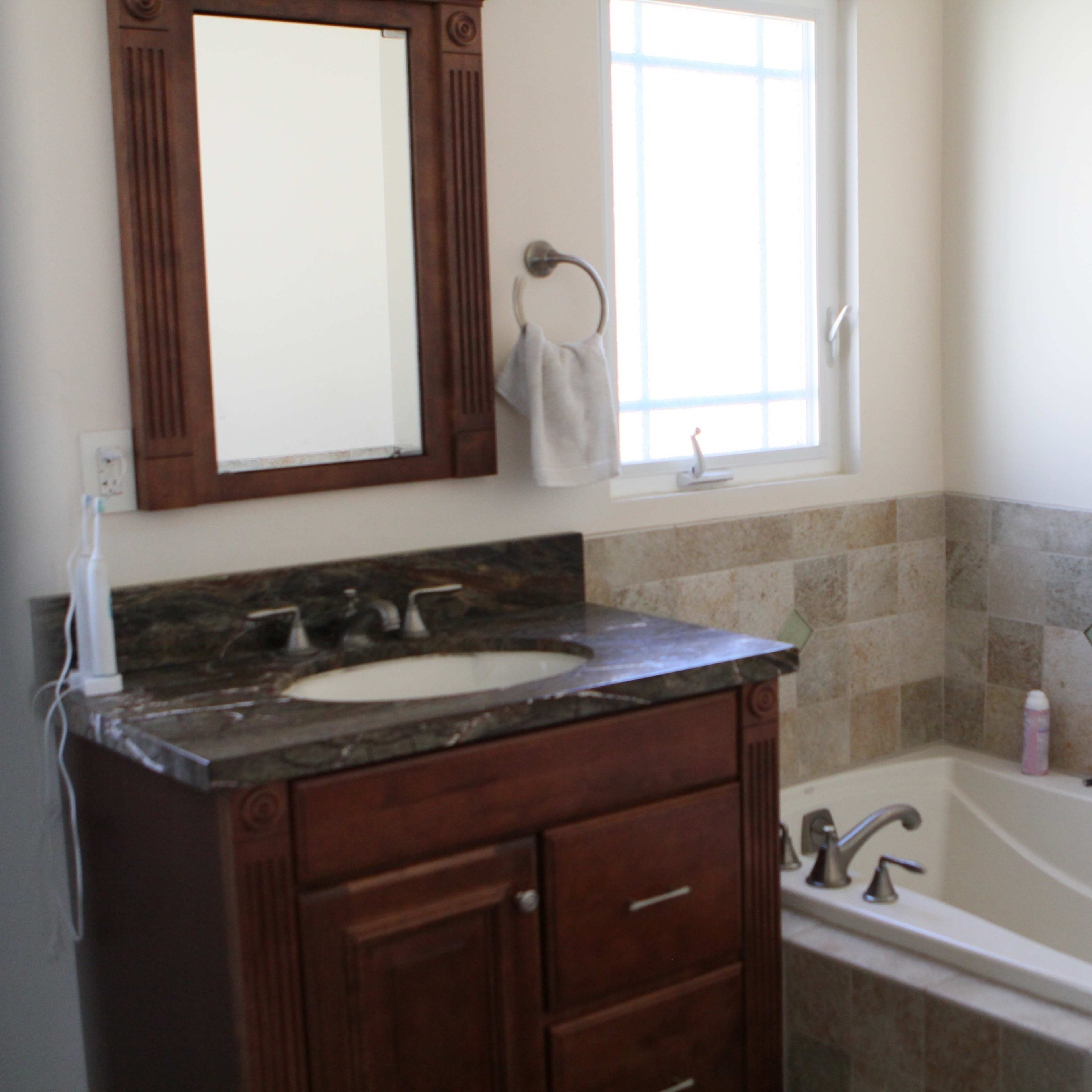 A bathroom features a sink with a wood cabinet, a large mirror, and a bathtub next to tiled walls with decorative accents.