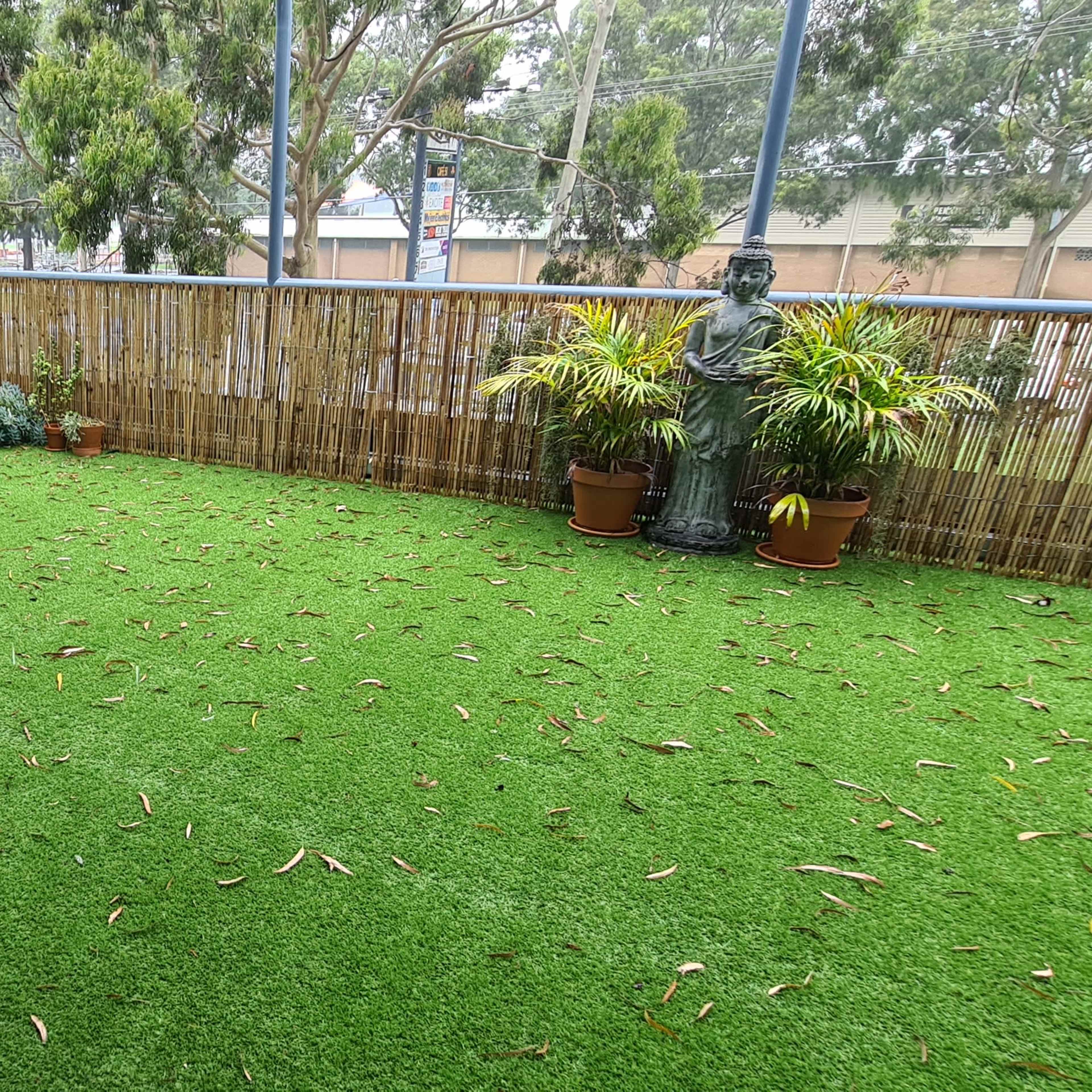 A covered outdoor area with artificial grass, surrounded by potted plants and a statue.
