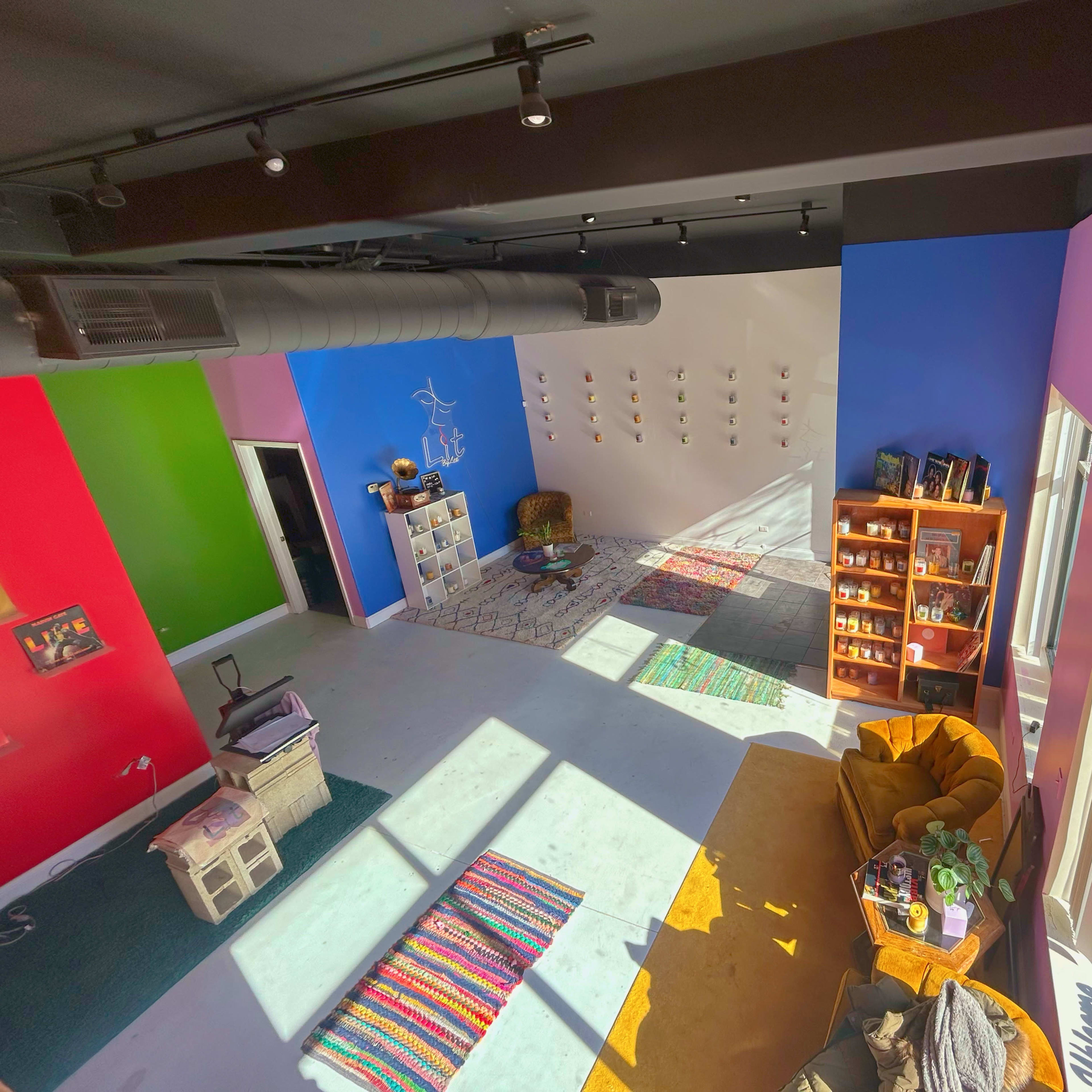 A brightly colored room with various seating areas, shelves filled with items, and a large window allowing natural light to enter.
