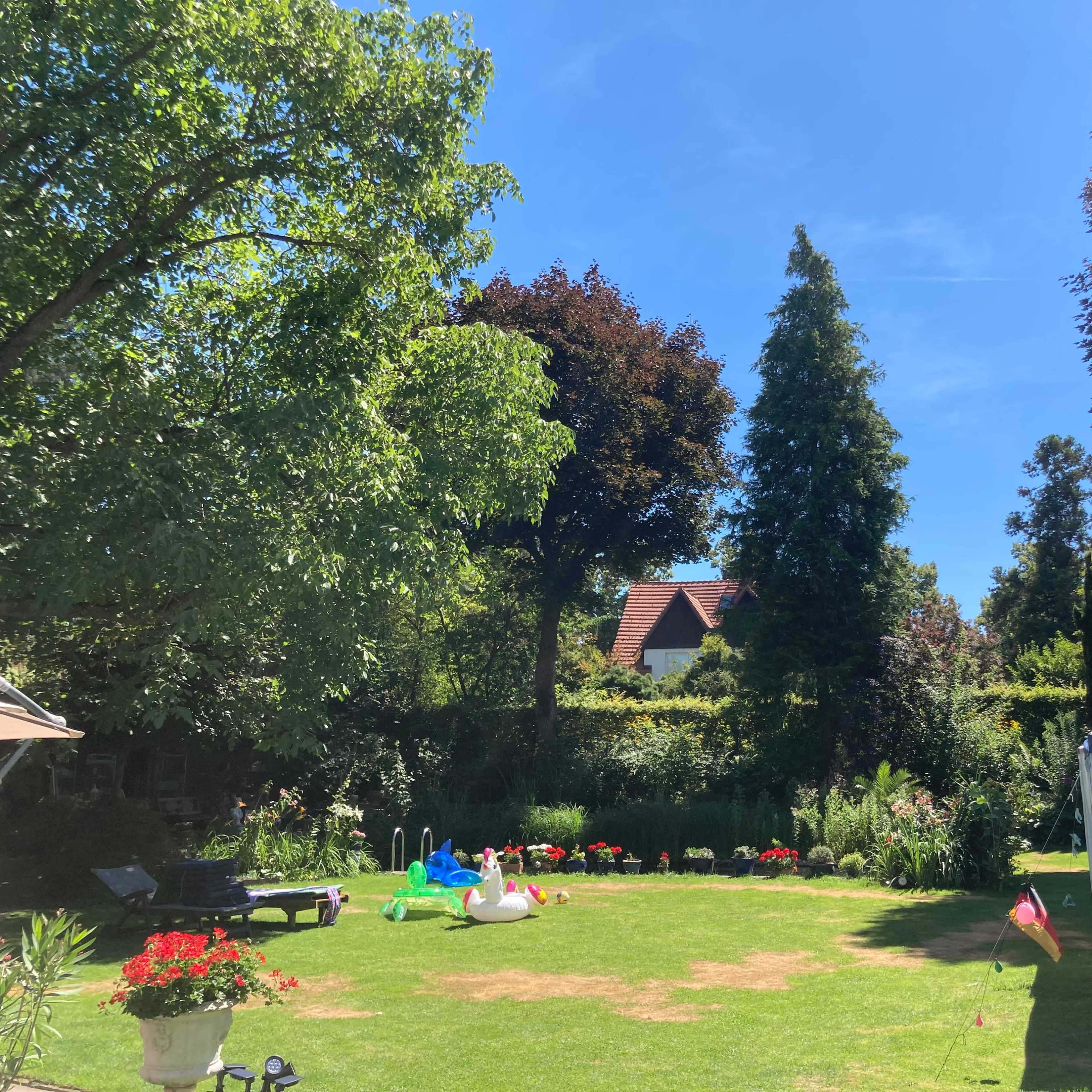 A lush garden features green grass, colorful flowers, and a gazebo under a clear blue sky.