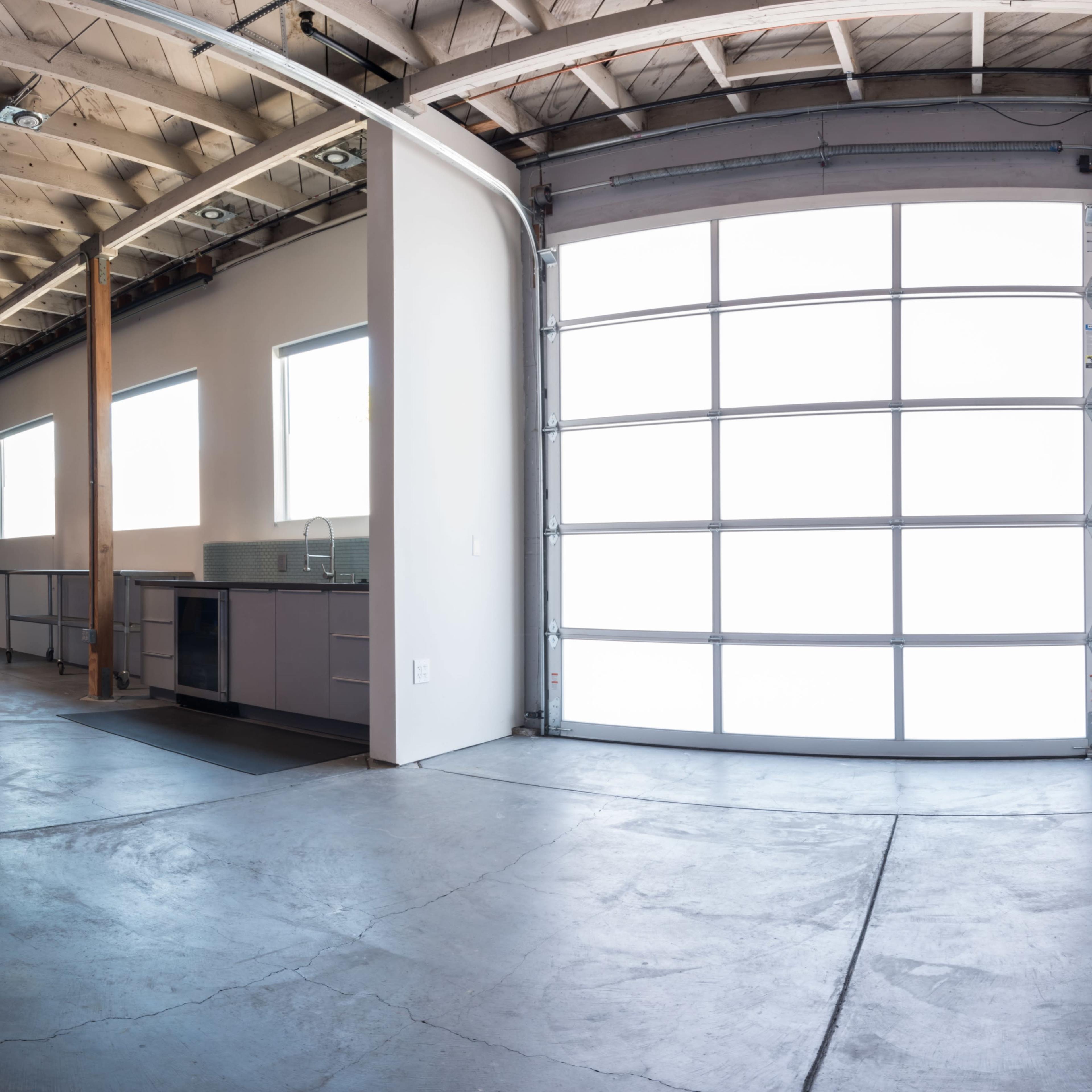 A spacious garage with a large glass panel door, a kitchen area on the left, and windows allowing natural light.