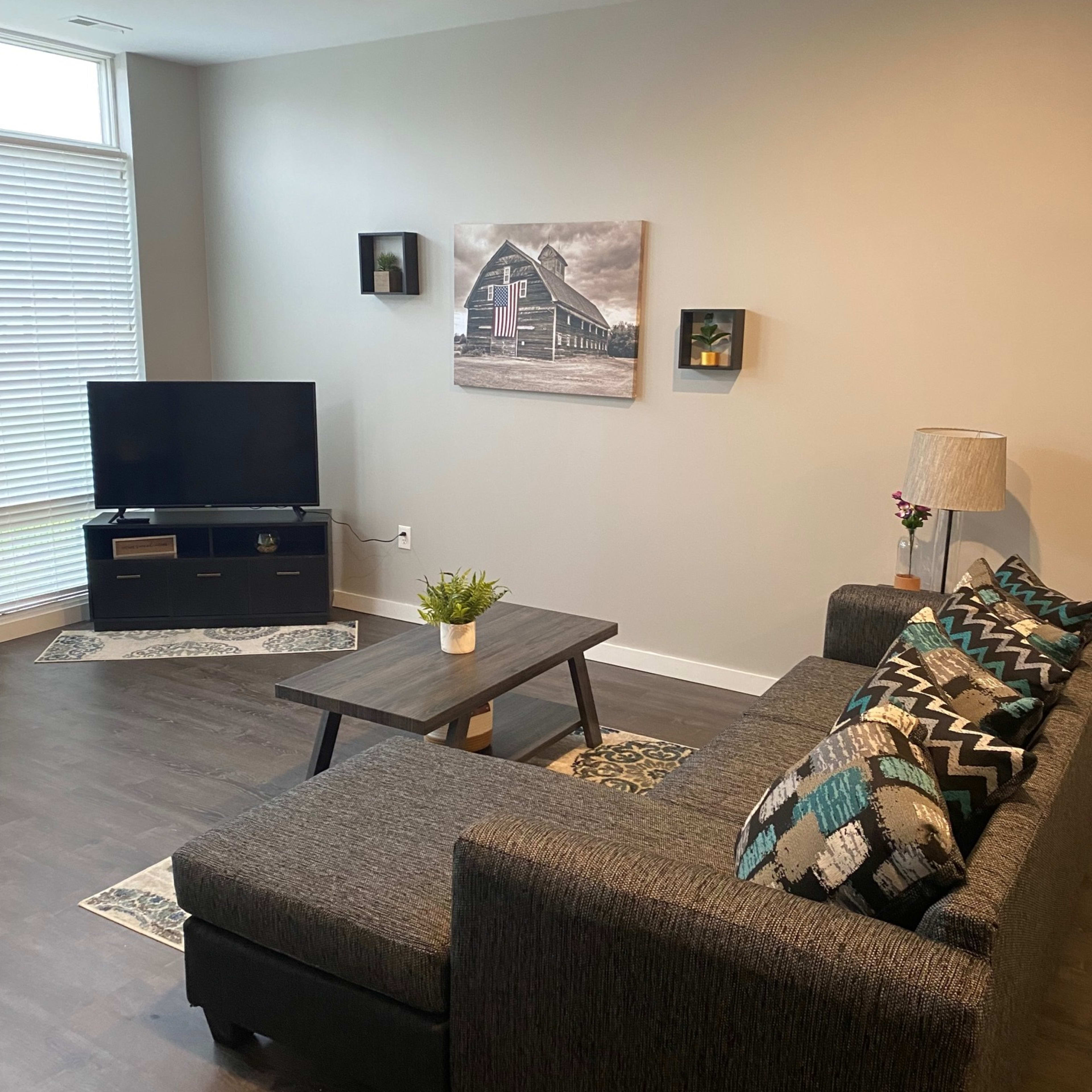 A modern living room with a grey sectional sofa, a black television stand holding a TV, and framed artwork on the walls.