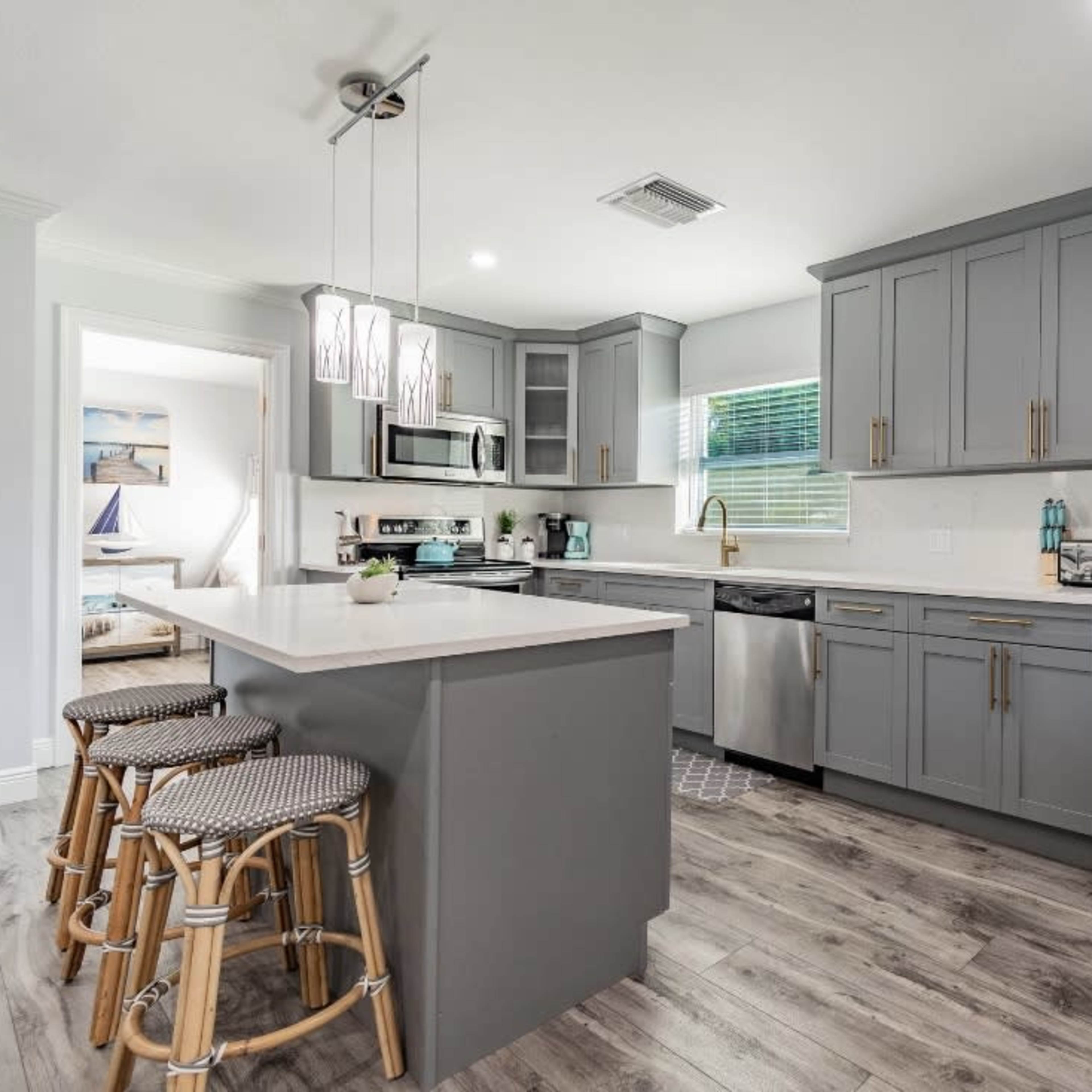 A modern kitchen featuring gray cabinets, stainless steel appliances, and a central island with three rattan barstools.