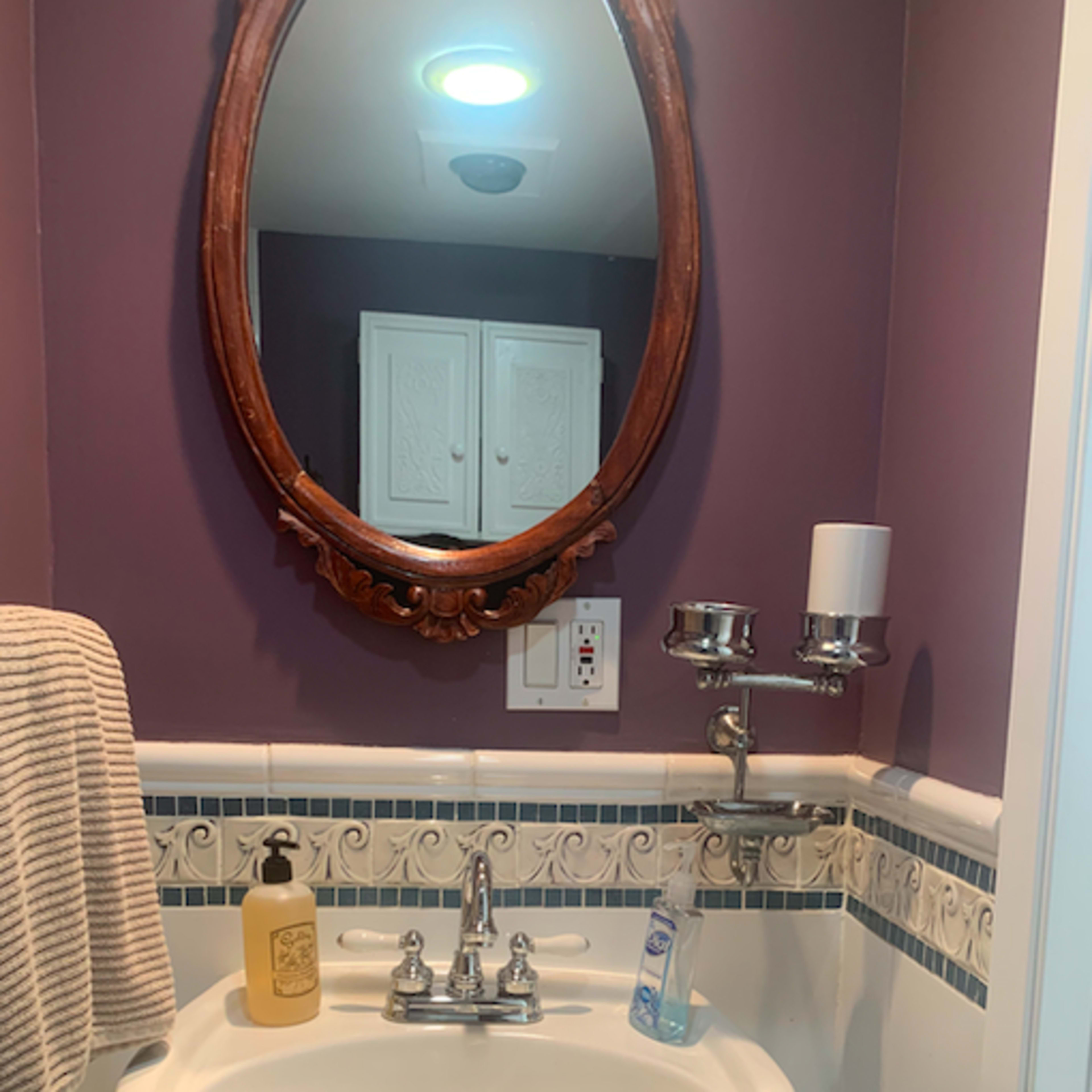 A small bathroom features a pedestal sink with a mirror above it, surrounded by purple walls and decorative tile.