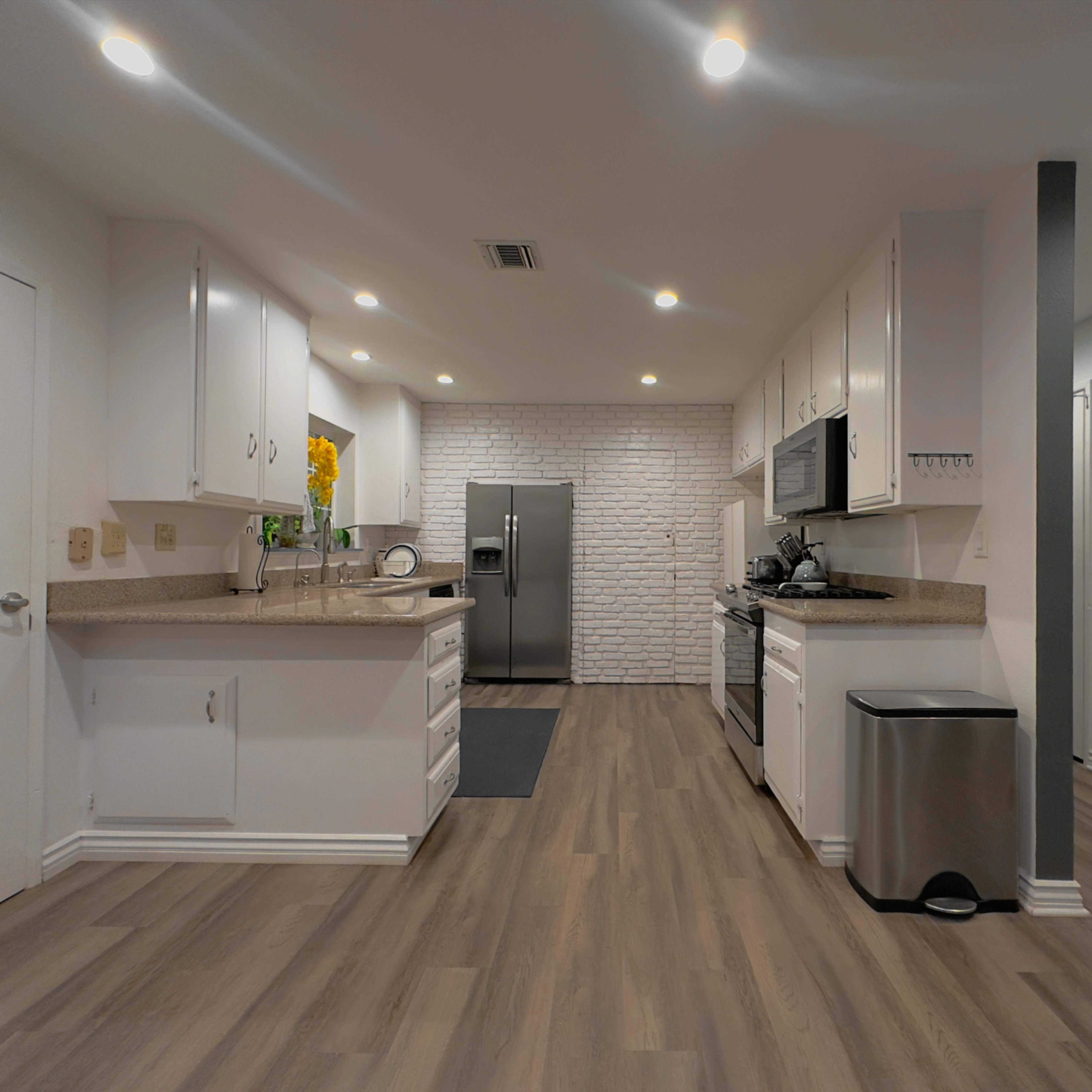 A modern kitchen features white cabinetry, stainless steel appliances, and a brick accent wall.
