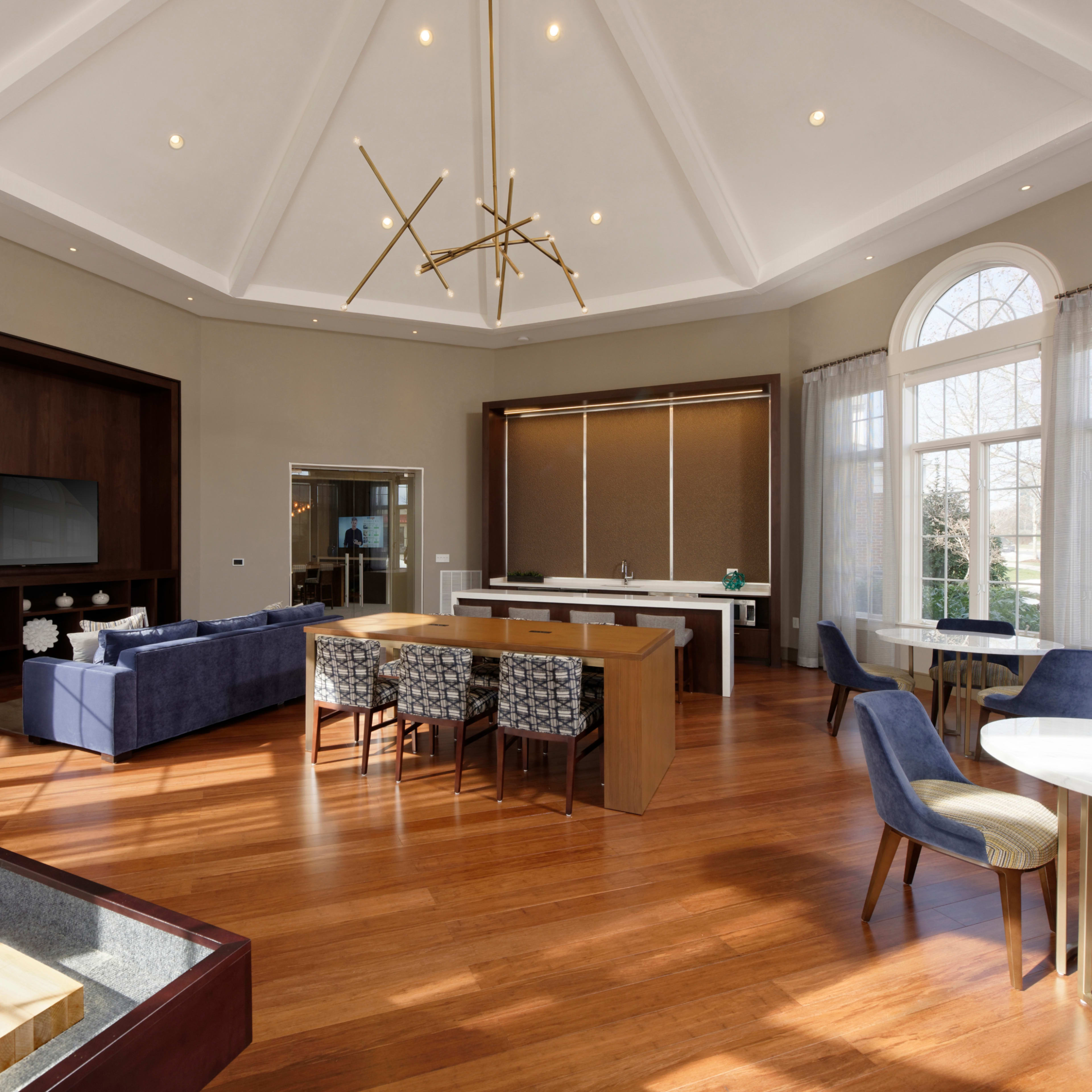A spacious and modern living area with a high ceiling, featuring a seating area, dining table, and large windows.