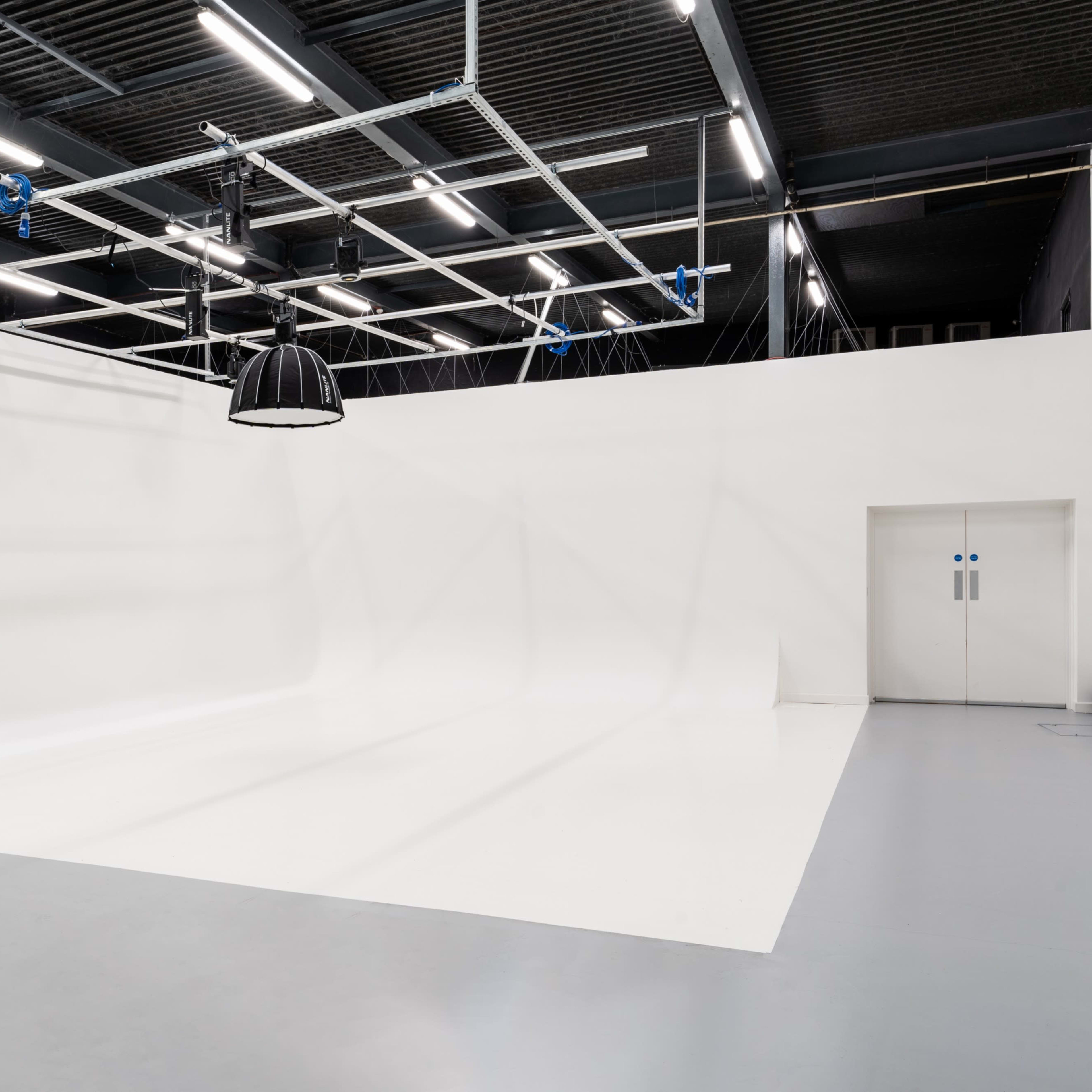 A spacious photography studio with a seamless white backdrop and a door marked with a restroom symbol.