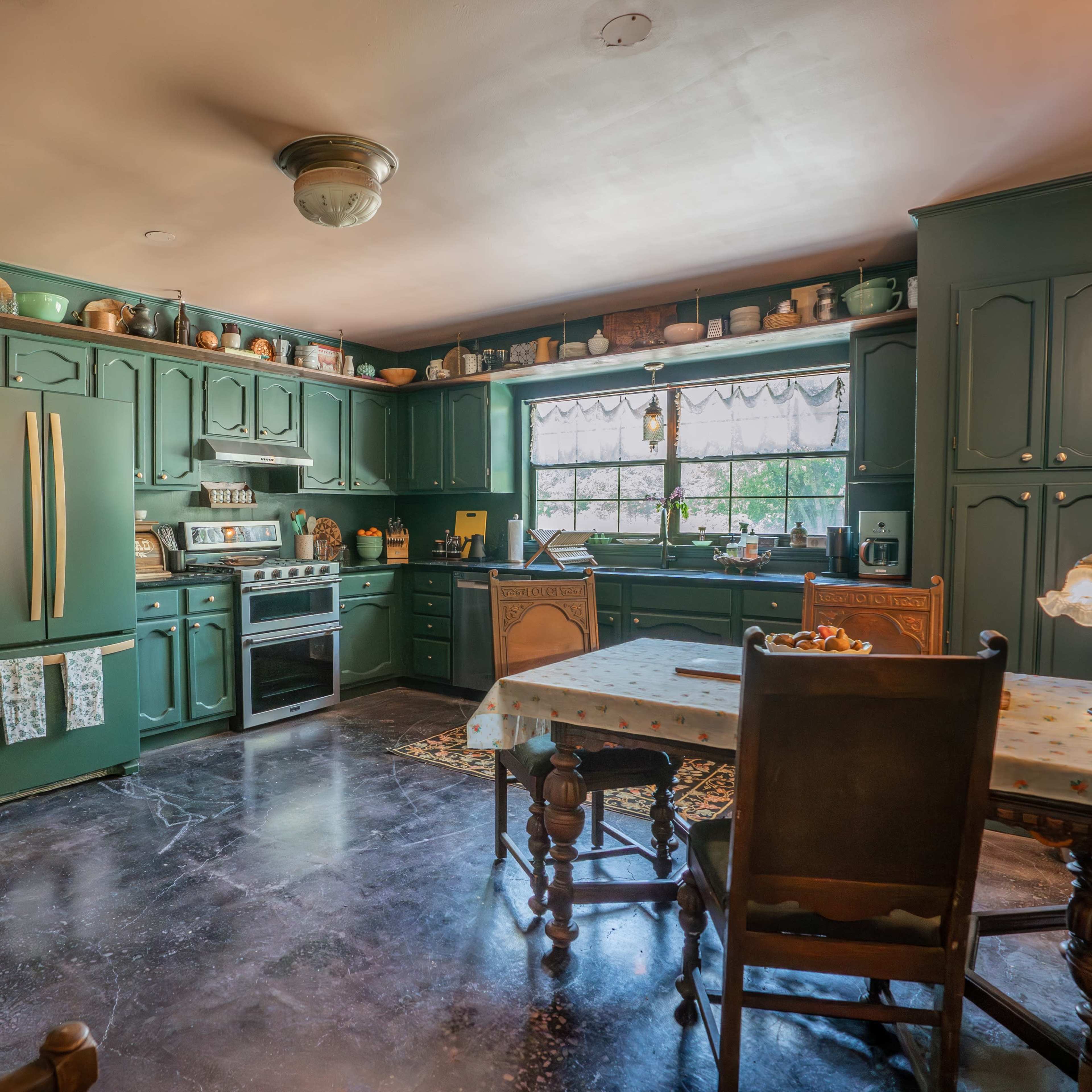 The kitchen features dark green cabinetry, a stainless steel stove, and a window above a sink with various jars and utensils neatly arranged on the shelves.