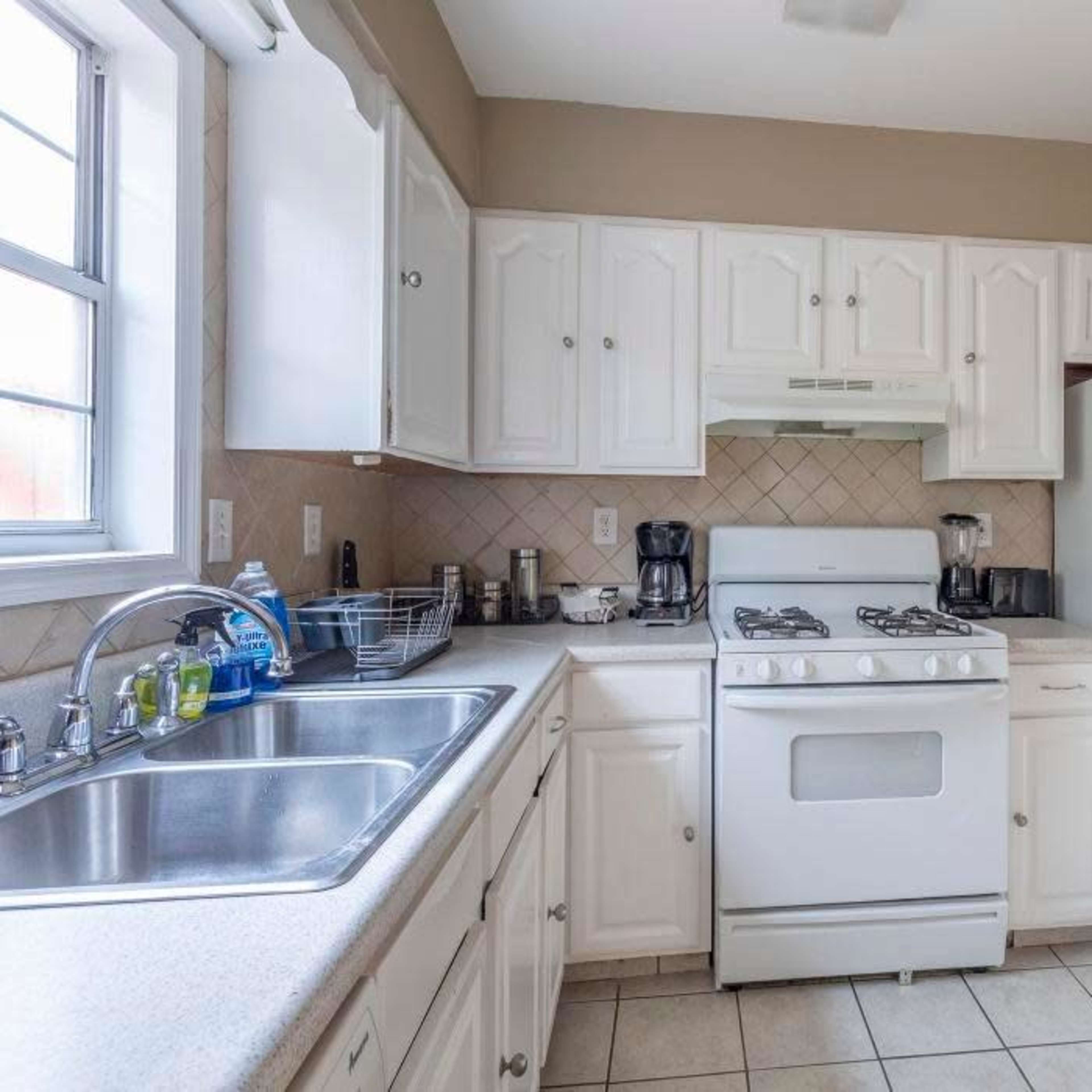 A kitchen featuring white cabinetry, a gas stove, a refrigerator, and a double sink with a window above it.