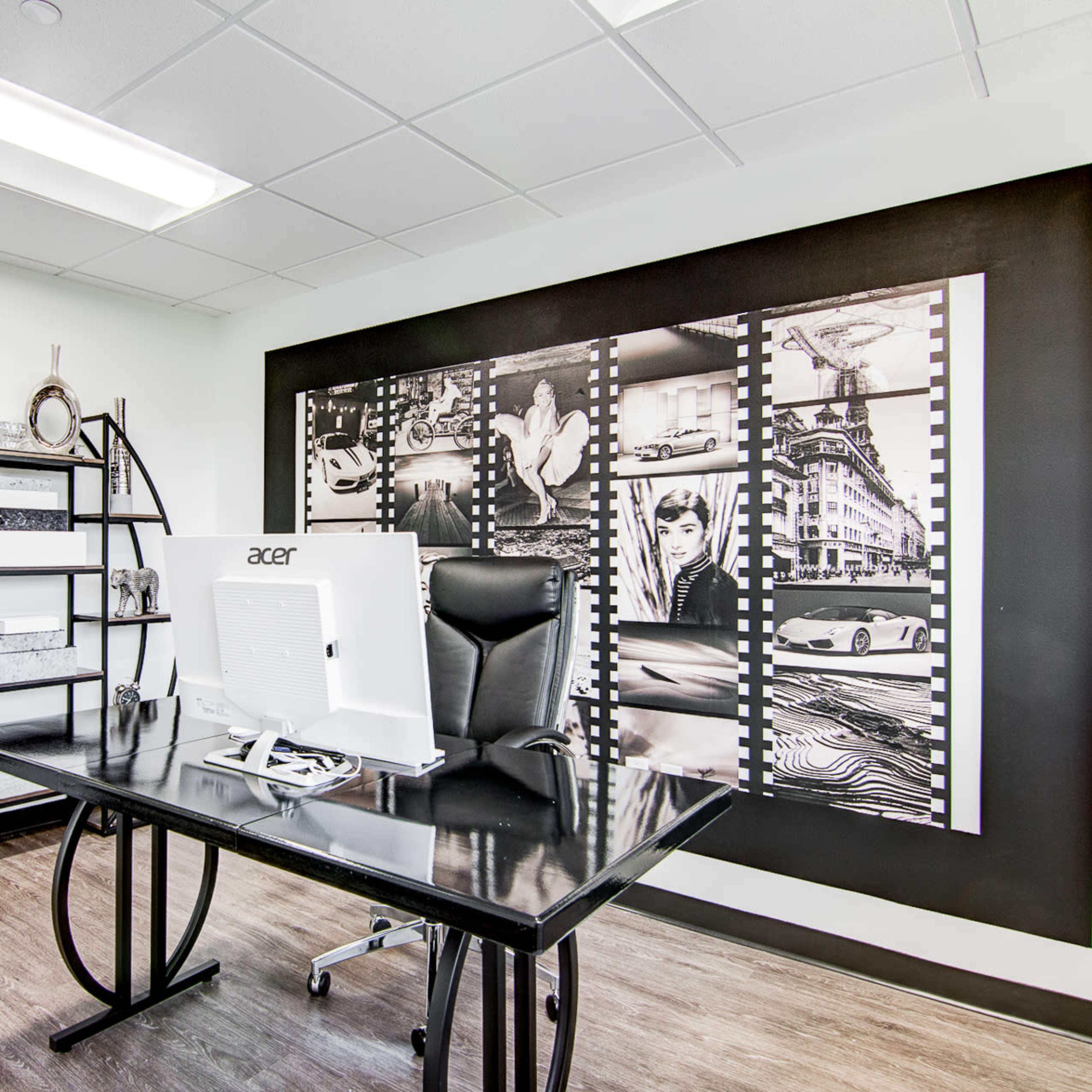 A modern office space featuring a black desk with a computer, a black office chair, and a decorative wall with a film strip design containing various images.