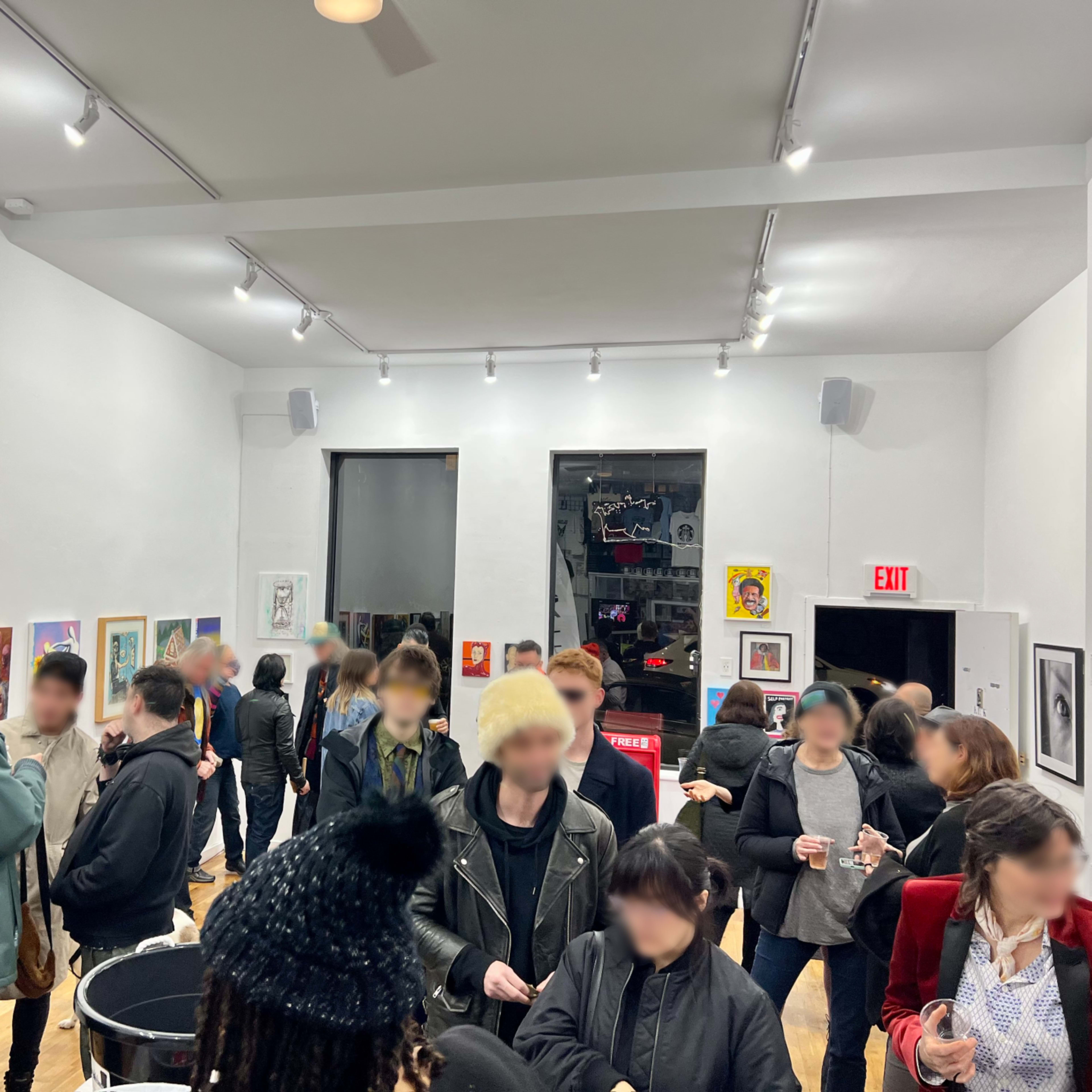 A crowd gathers in a gallery space adorned with various artworks on the white walls.