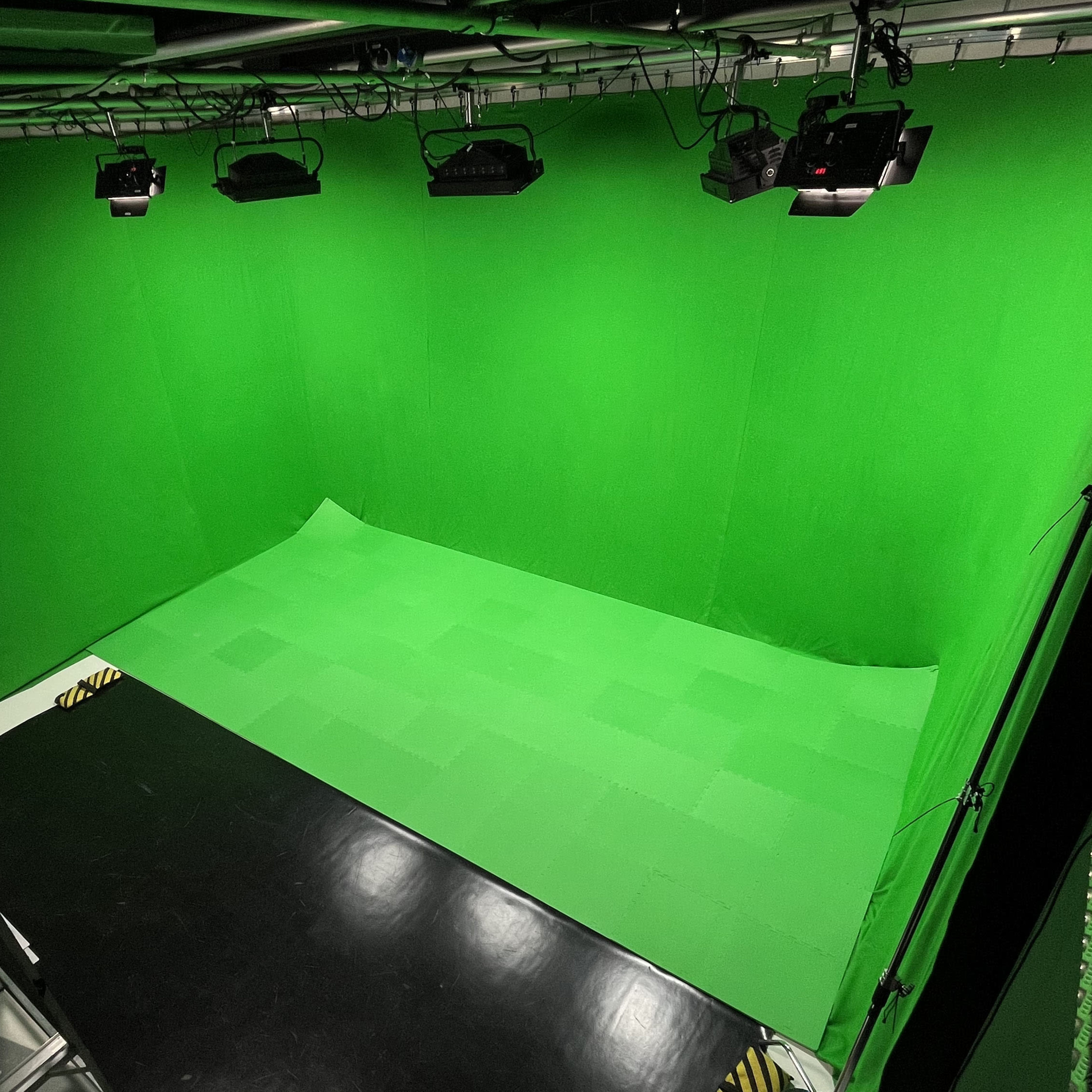A studio space with a green backdrop and lighting fixtures, designed for filming or photography.