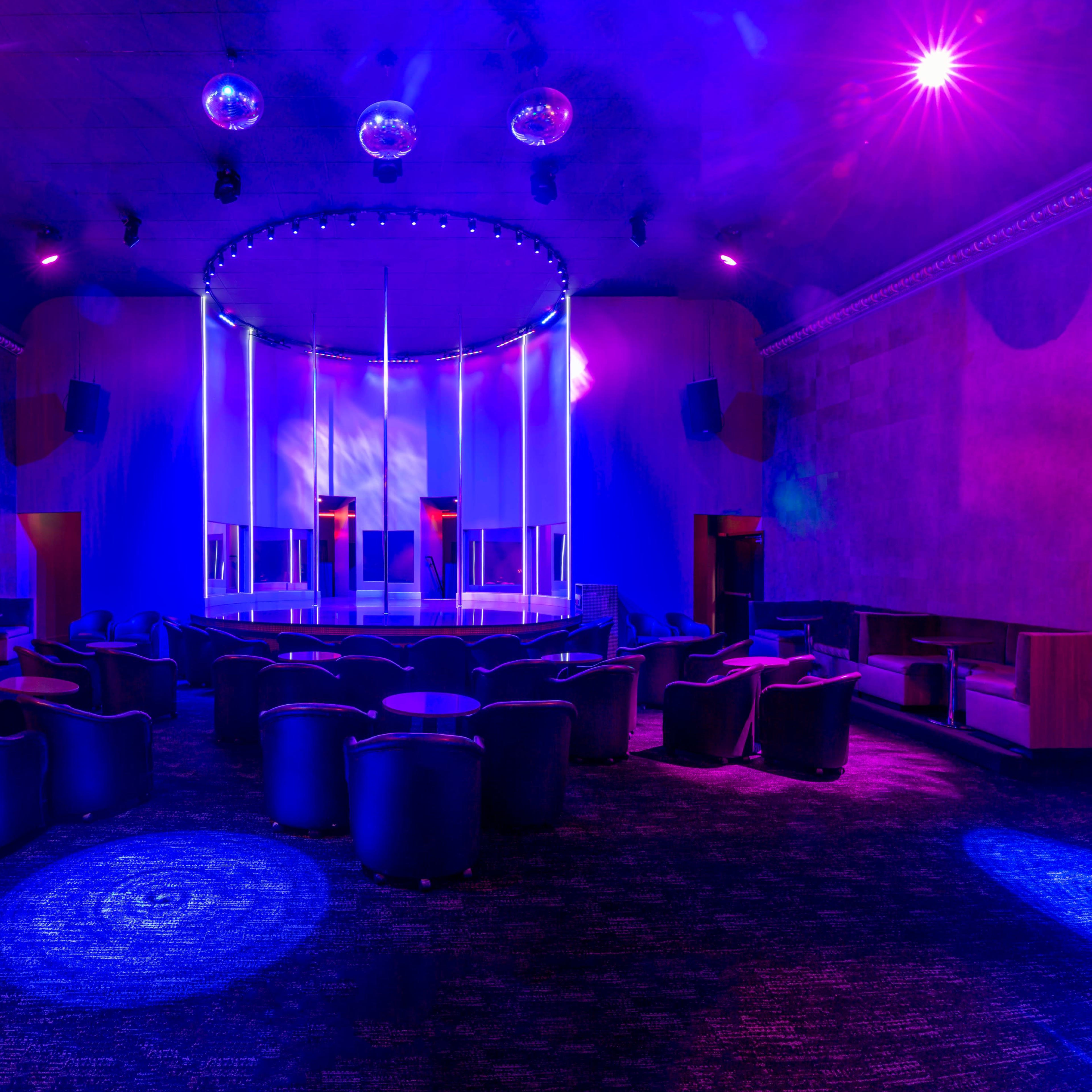 A dimly lit, modern nightclub interior with circular seating and illuminated disco balls hanging from the ceiling.