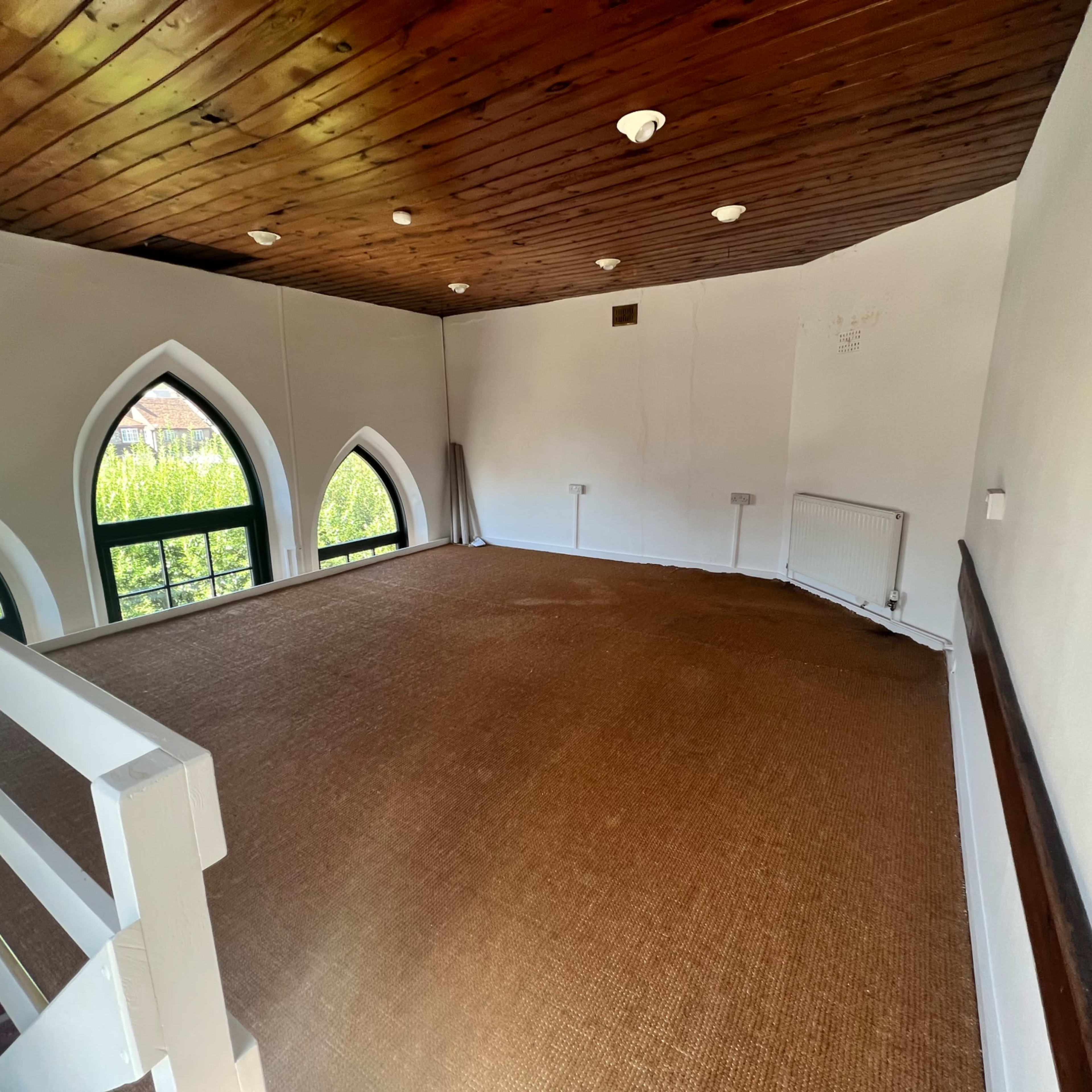 An empty room with a wooden ceiling, large arched windows, and a carpeted floor.