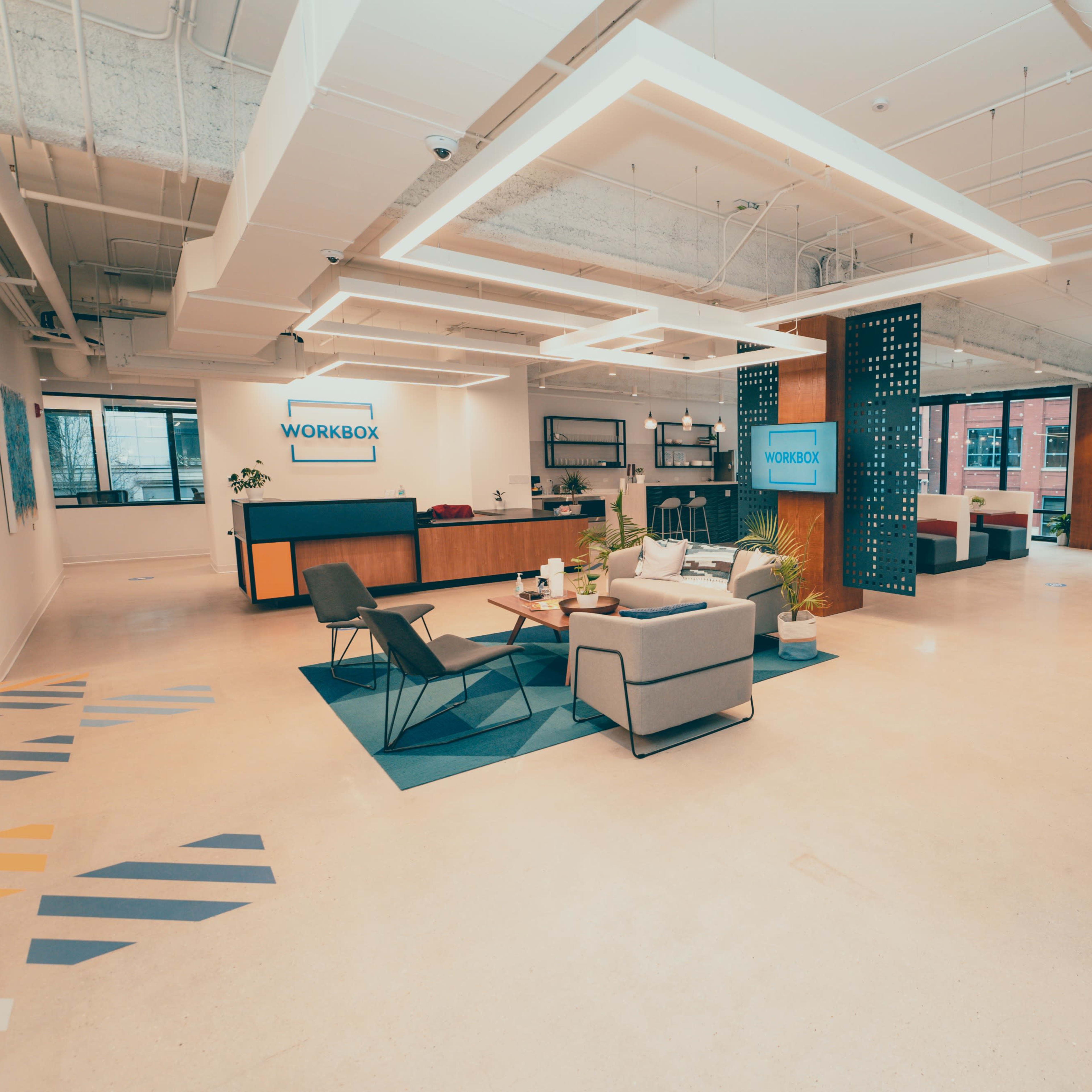 A modern office space with a reception area featuring seating, a coffee table, and a workspace with tables and chairs.