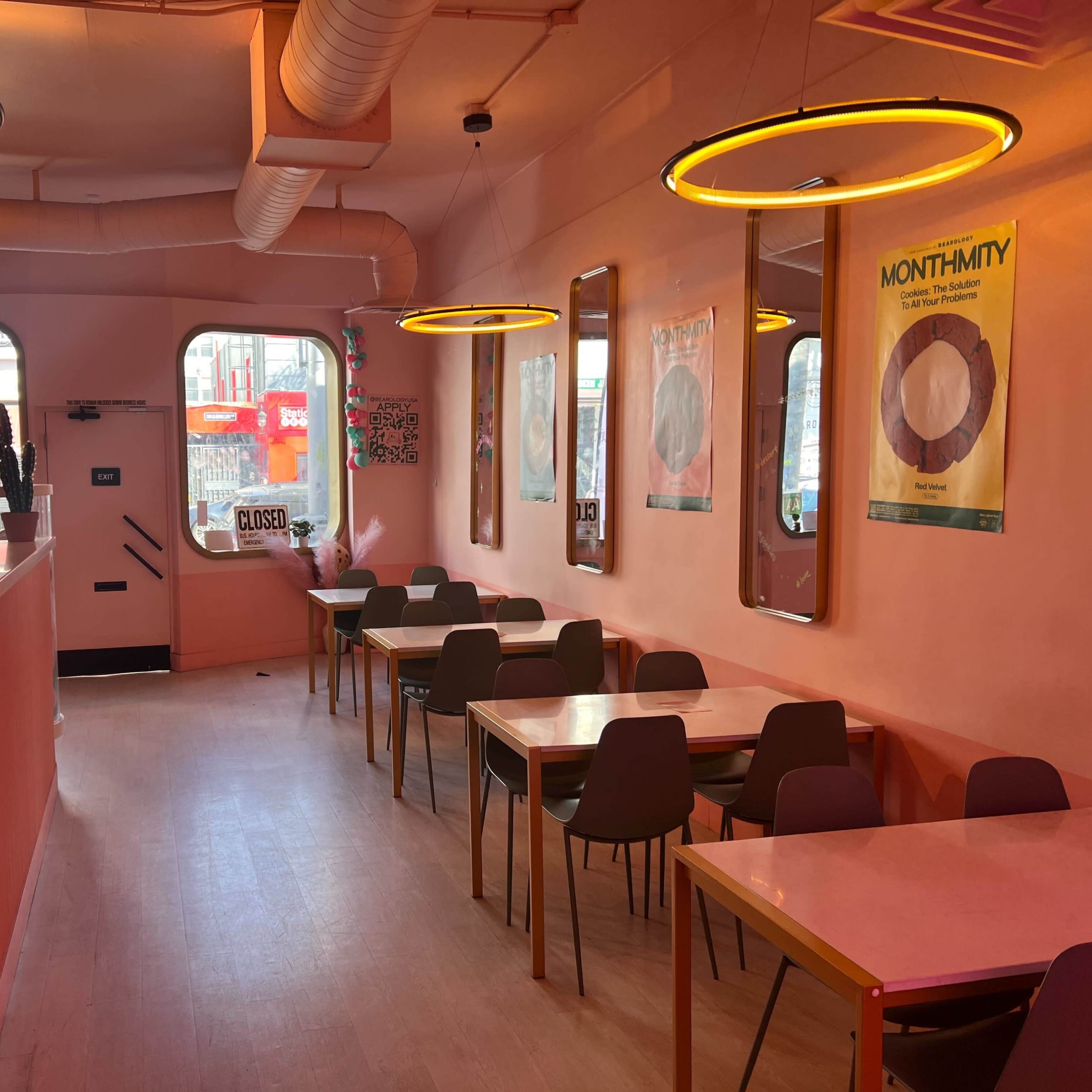 The interior of a café features pink walls, wooden tables, and circular lights, with a view of the street through large windows.