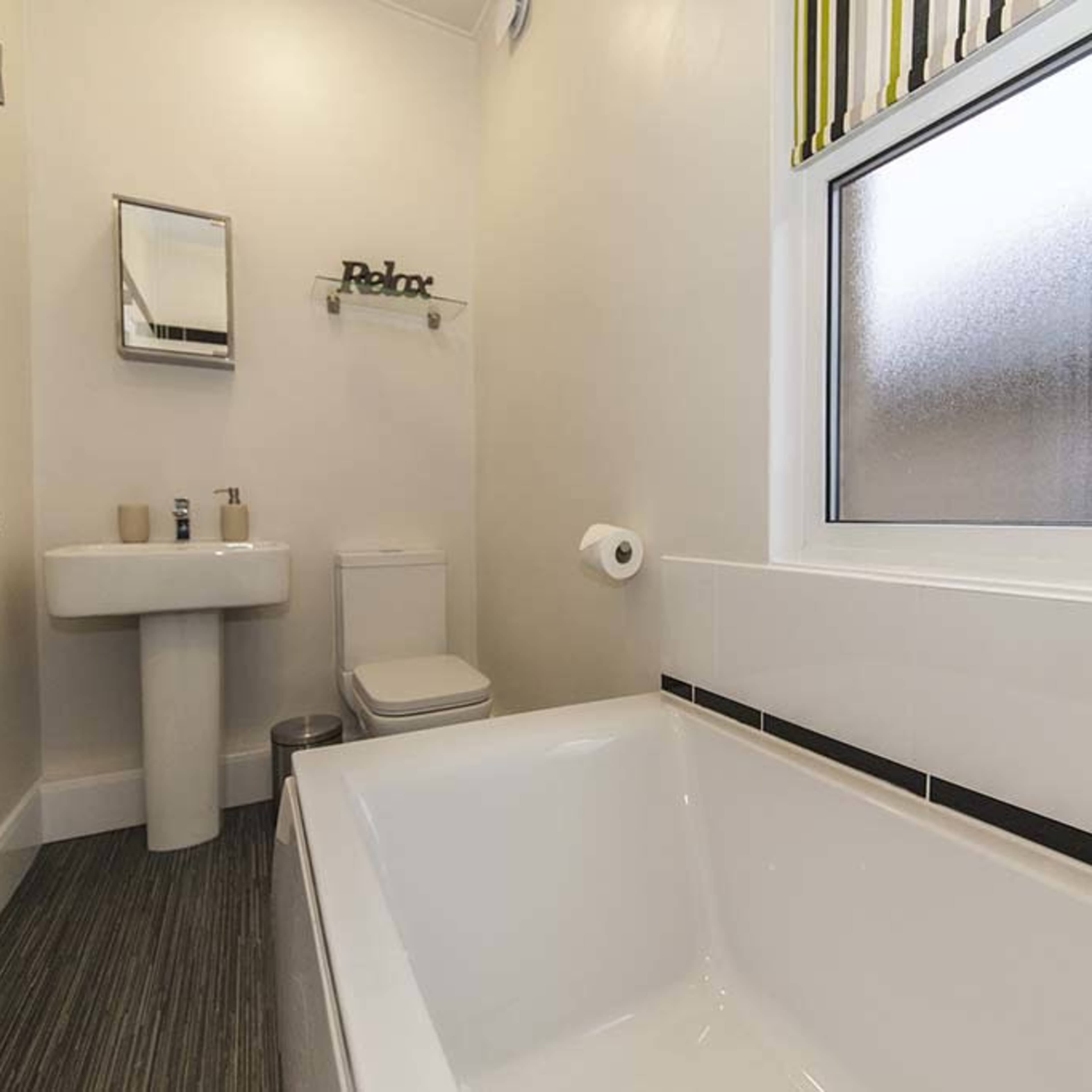 A modern bathroom featuring a bathtub, a toilet, and a sink against white walls with a frosted window.