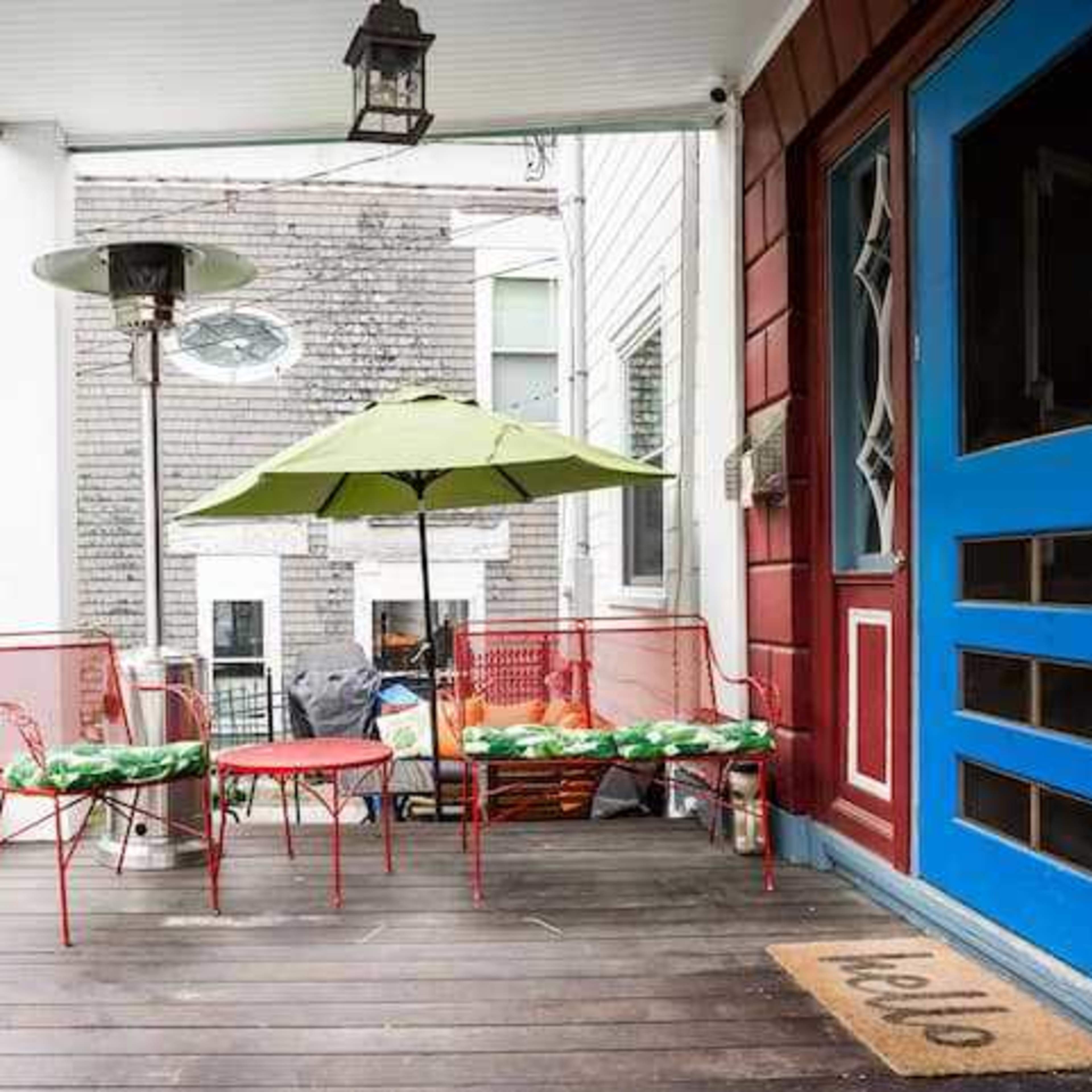 A porch with a blue door, red metal chairs, a round table, an umbrella, and a welcome mat.