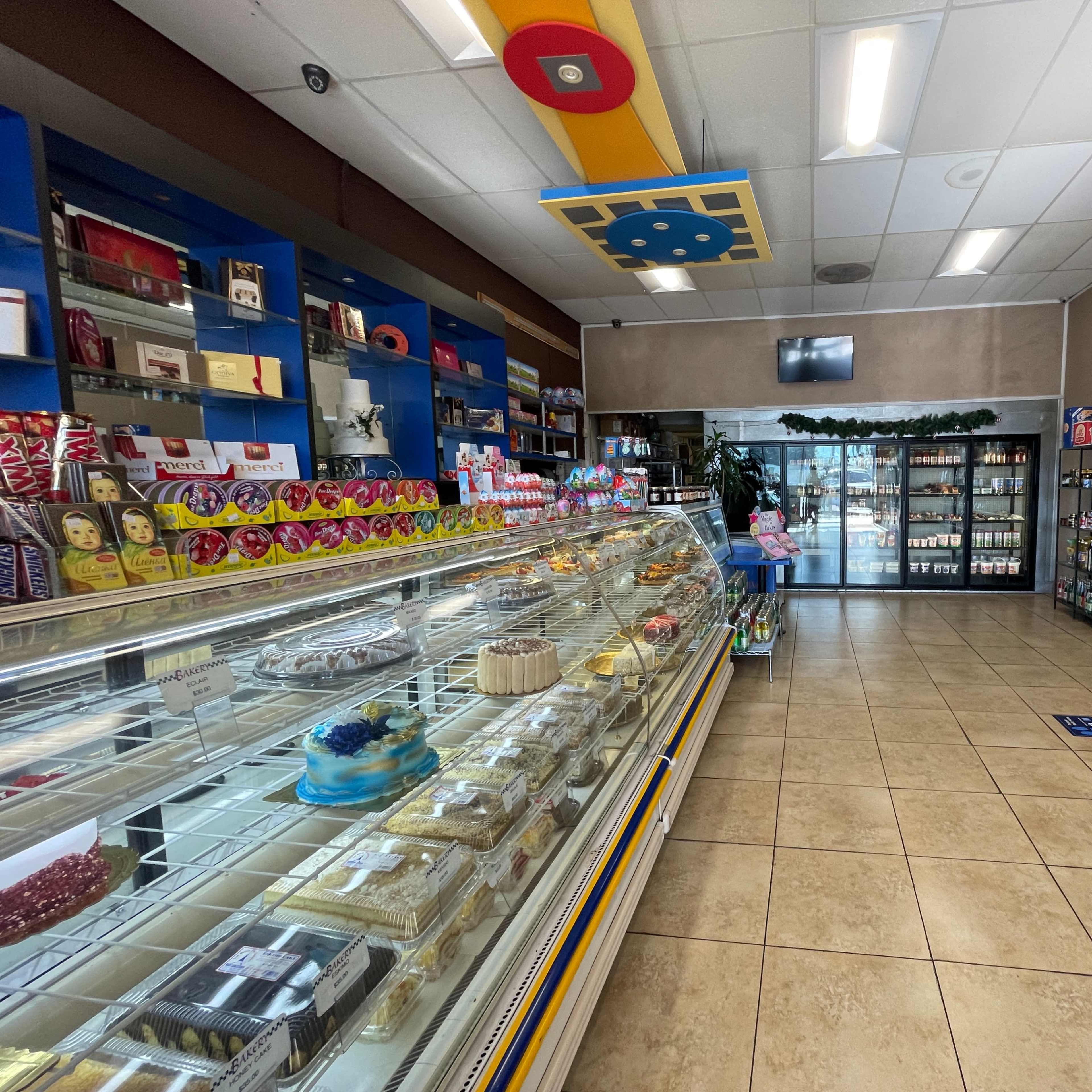 The interior of a shop featuring a display case with various desserts on the left and shelves stocked with packaged goods on the right.