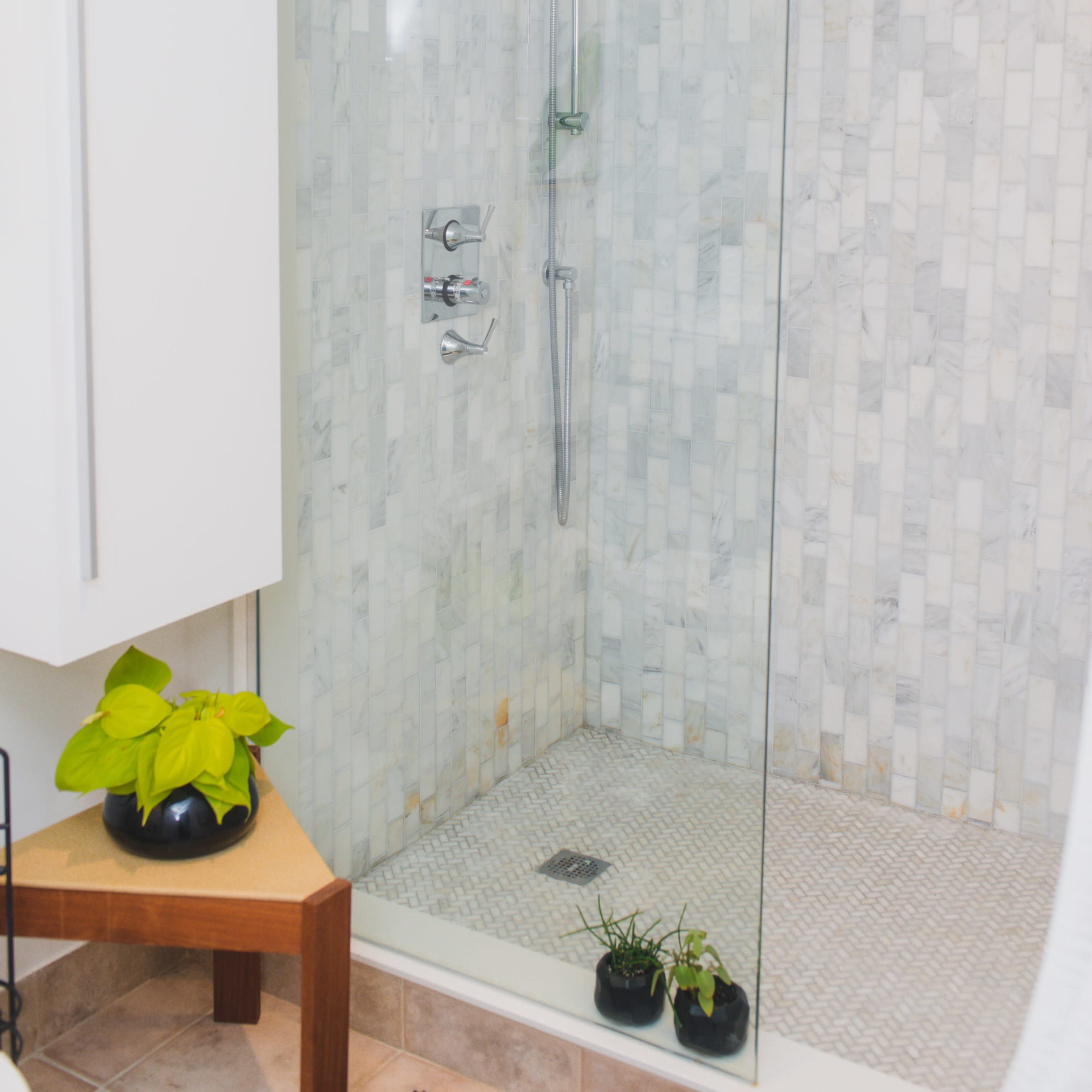 A modern shower with a glass enclosure, marble walls, and a tiled floor, featuring a showerhead and a handheld shower fixture.