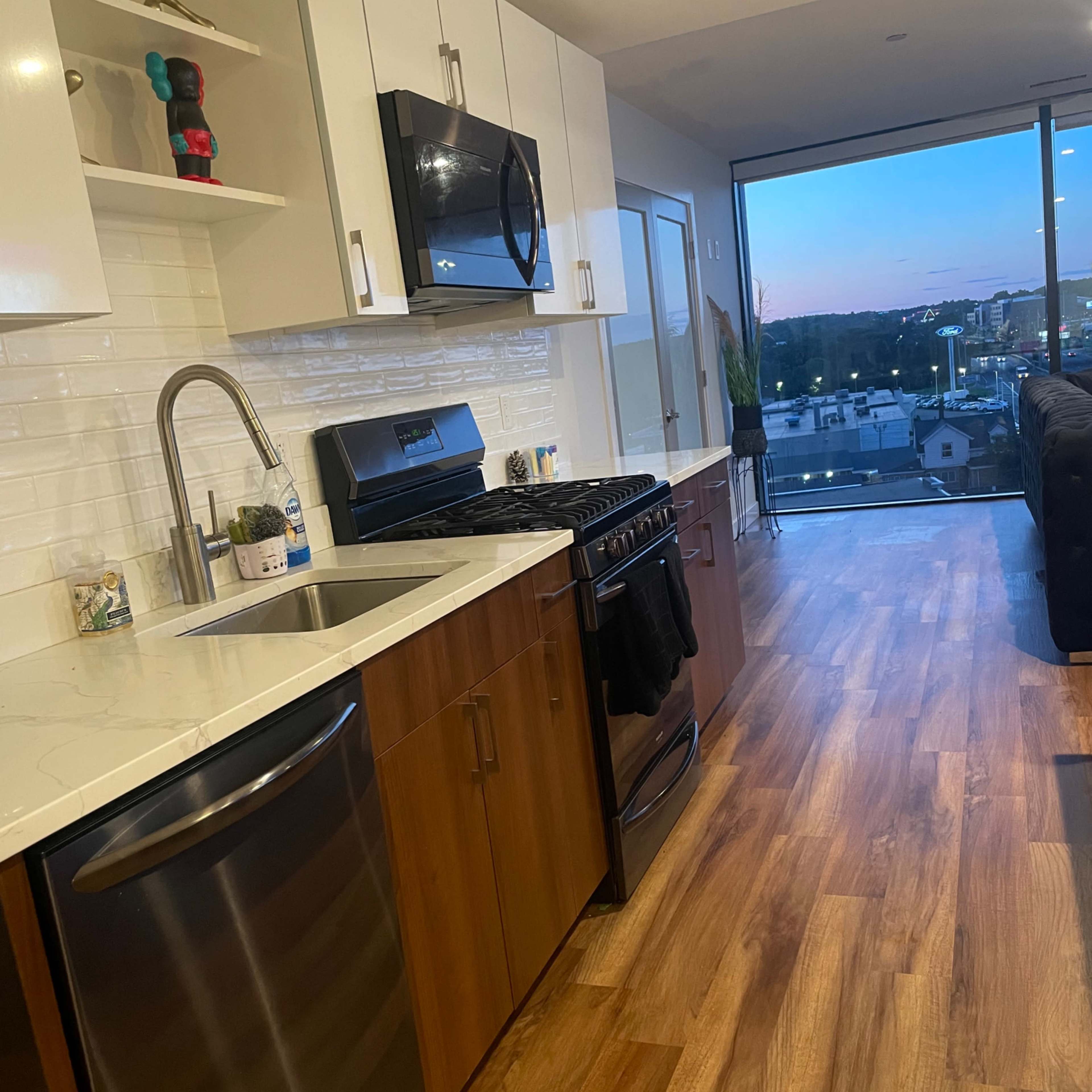 A modern kitchen with wooden cabinets, stainless steel appliances, and a large window overlooking an outdoor view.